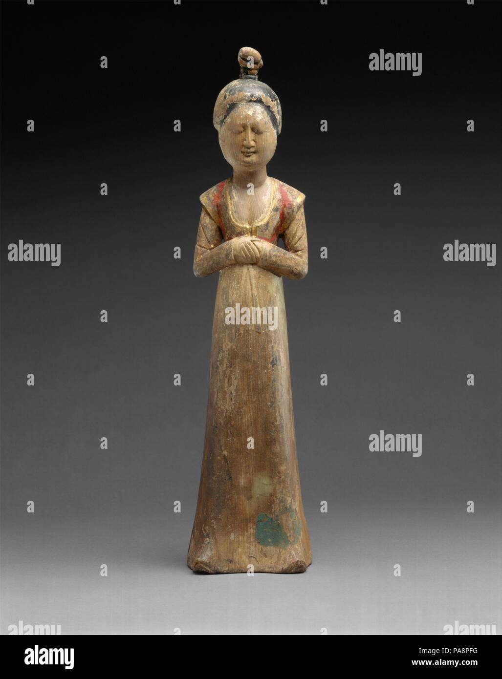 Standing Female Attendant. Culture: China. Dimensions: H. 21 in. (53.3 cm). Date: late 7th century-early 8th century.  This rare surviving example of a tomb figurine carved from wood must have come from the dry regions of the Silk Road, but displays the fashionable high-waisted dress and short jacket of the Tang court style. Museum: Metropolitan Museum of Art, New York, USA. Stock Photo