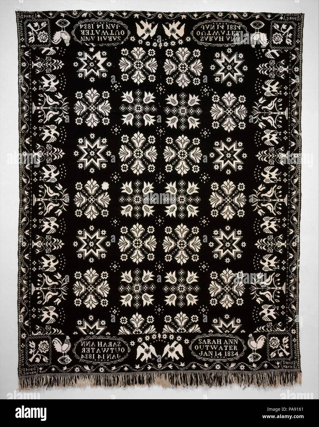 Coverlet. Culture: American. Dimensions: 98 3/8 x 75 in. (249.9 x 190.5 cm). Maker: David Daniel Haring (1800-1889). Date: 1834.  This dark blue wool and undyed cotton double cloth coverlet is woven in two panels and seamed at the center. Floral and star motifs typically found in Haring's work decorate the central field. The left and right borders have images of eagles with outspread wings alternating with vases of flowers and pairs of birds in trees. From left to right along each panel of the top and bottom borders, there is a rooster standing on an egg, the inscription cartouche, and an eagl Stock Photo