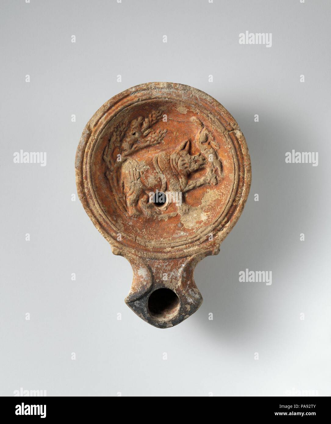 Terracotta oil lamp. Culture: Roman, Cypriot. Dimensions: Overall: 1 1/8 x 4 in. (2.9 x 10.2 cm). Date: 1st half of 1st century A.D..  On the discus a rhinoceros is shown tossing with its horn a large cat, probably a lion, while a small animal, possibly meant to be a baby rhino, hides in a tree behind. The rhinoceros, unknown in the Mediterranean world before Roman times, is only rarely depicted in Roman art and on coins; it is shown, for example, on the Roman mosaic from Lod, Israel. The base is inscribed FAVSTI ([of the lamp maker] Faustus); he seems to have worked in Italy, Egypt, and Petra Stock Photo