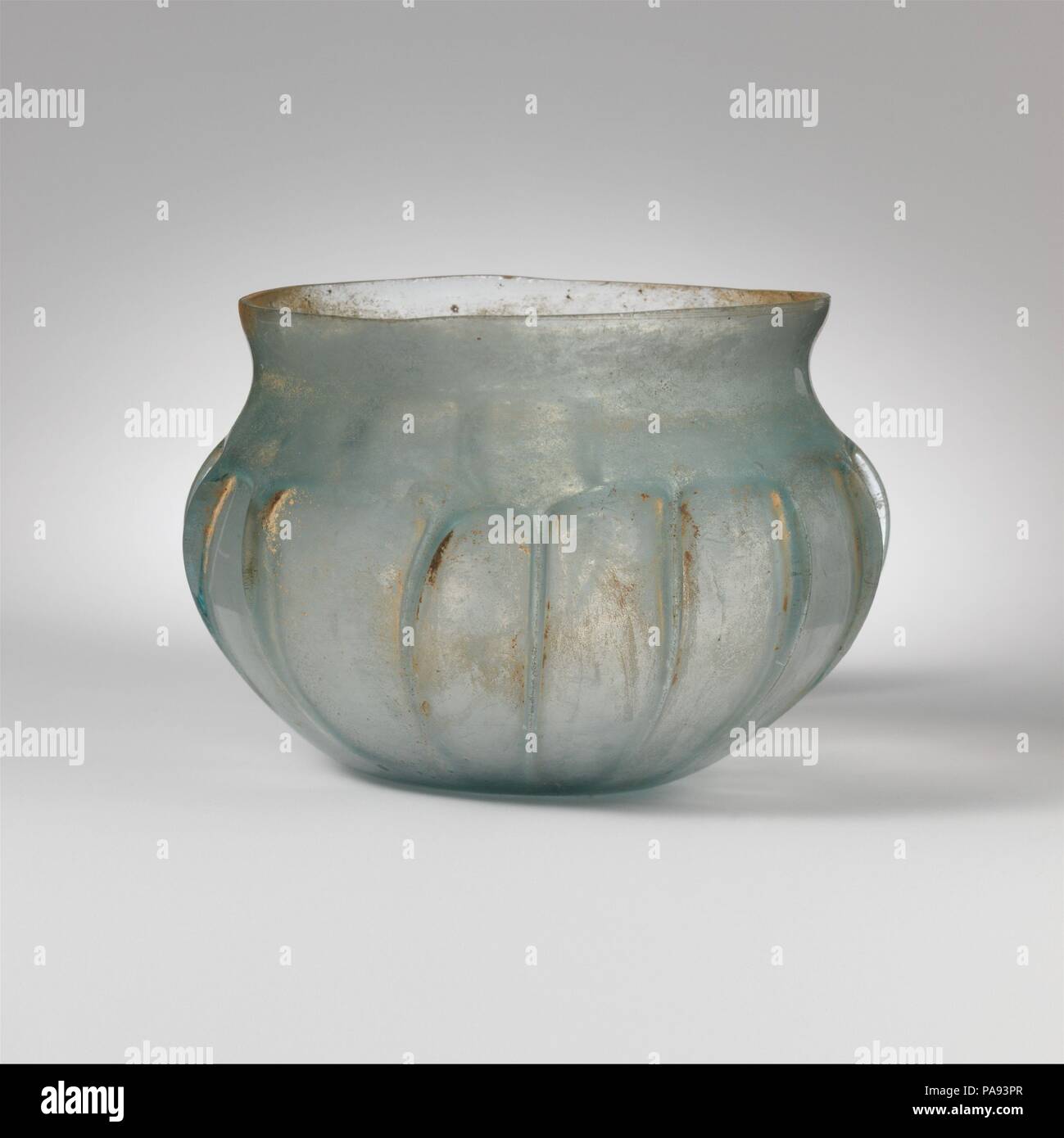 Glass ribbed bowl. Culture: Roman. Dimensions: H.: 3 in. (7.6 cm)  Diam.: 4 3/8 in. (11.1 cm). Date: mid-1st century A.D..  Translucent light blue green.  Knocked-off, uneven, ground rim; concave neck; globular body curving in to thick, flat bottom.  Side tooled into fifteen irregular, vertical ribs, with arched projections around shoulder above tops.  Intact; pinprick bubbles; dulling, patches of brownish weathering, and faint iridescence.  Greenish ribbed bowl. Museum: Metropolitan Museum of Art, New York, USA. Stock Photo