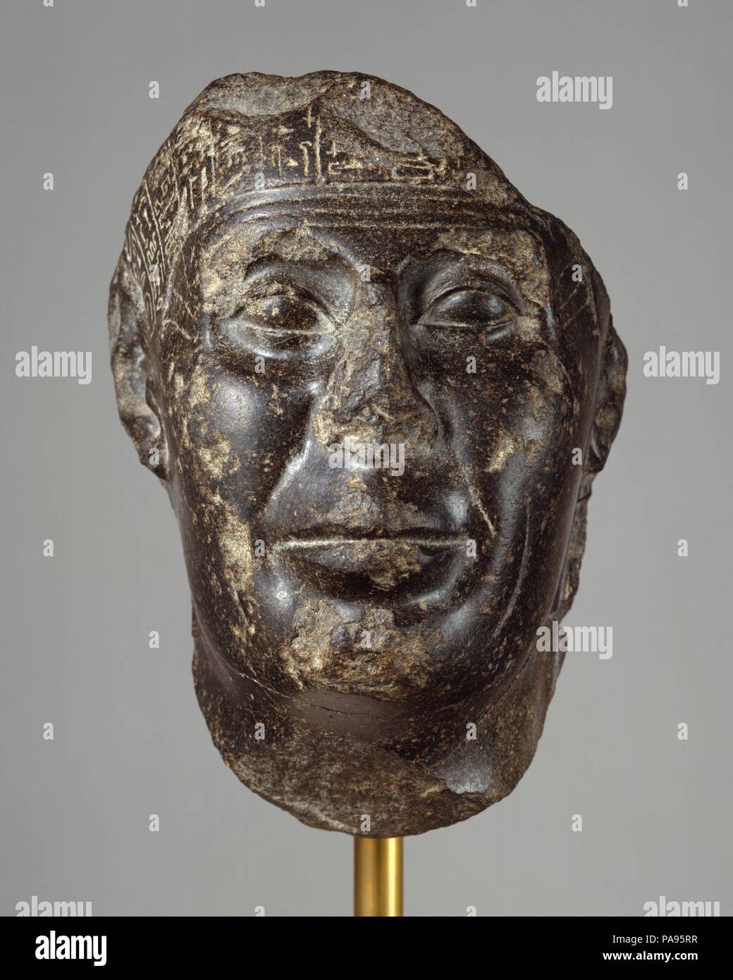 Head from a Statue with Magical Texts. Dimensions: H. 21.2 cm (8 3/8 in.); W. 14.5 cm (5 11/16 in.); D. 11.5 cm (4 1/2 in.). Dynasty: Dynasty 30. Reign: probably reign of Nectanebo II. Date: probably 360-343 B.C..  Magical texts like those on the Metternich stela (50.85) probably covered all but the face, feet, and hands of the statue to which this fragment belonged.  The statue would have stood in a temple where it could be visited by persons wishing to be healed.  Inscribed statues of this type can almost all be dated to the fourth century.  A man well-advanced in years is depicted, his skin Stock Photo