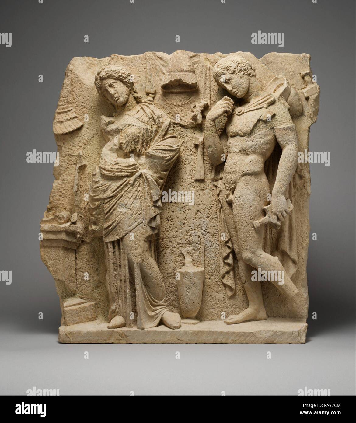 Limestone funerary relief. Culture: Greek, South Italian, Tarentine. Dimensions: H. 23 1/16 in. (58.5 cm); width as preserved 21 1/8 in. (53.6 cm). Date: ca. 325-300 B.C..  Tarentum (modern Taranto) was a wealthy Greek colony on the southeast coast of Italy, a pivotal location along the trade routes between Greece and Italy. During the fourth century B.C., ostentatious grave monuments in the form of small temple-like buildings decorated with painted sculpture filled the city cemetery. This relief must come from such a building. It represents a young warrior and a woman standing by an altar. Be Stock Photo