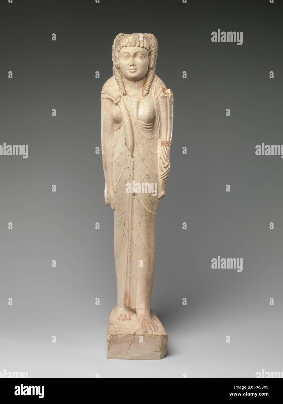 Statuette of Arsinoe II for her Posthumous Cult. Dimensions: H. 38.7 cm (15 1/4 in); W. 9.6 cm (3 3/4 in); D. 13.2 cm (5 3/16 in). Date: ca. 150-100 B.C..  The inscription on the back of this figure refers to Queen Arsinoe II as a goddess, indicating it was made after 270 B.C. when her cult was established at the time of her death in by her brother and husband, Ptolemy II. Gilding indicating divinity once covered her face, and traces still remain at the edges of her neckline.   While the overall frontal pose and disposition of the limbs in this small statue follows Egyptian traditions, the cor Stock Photo