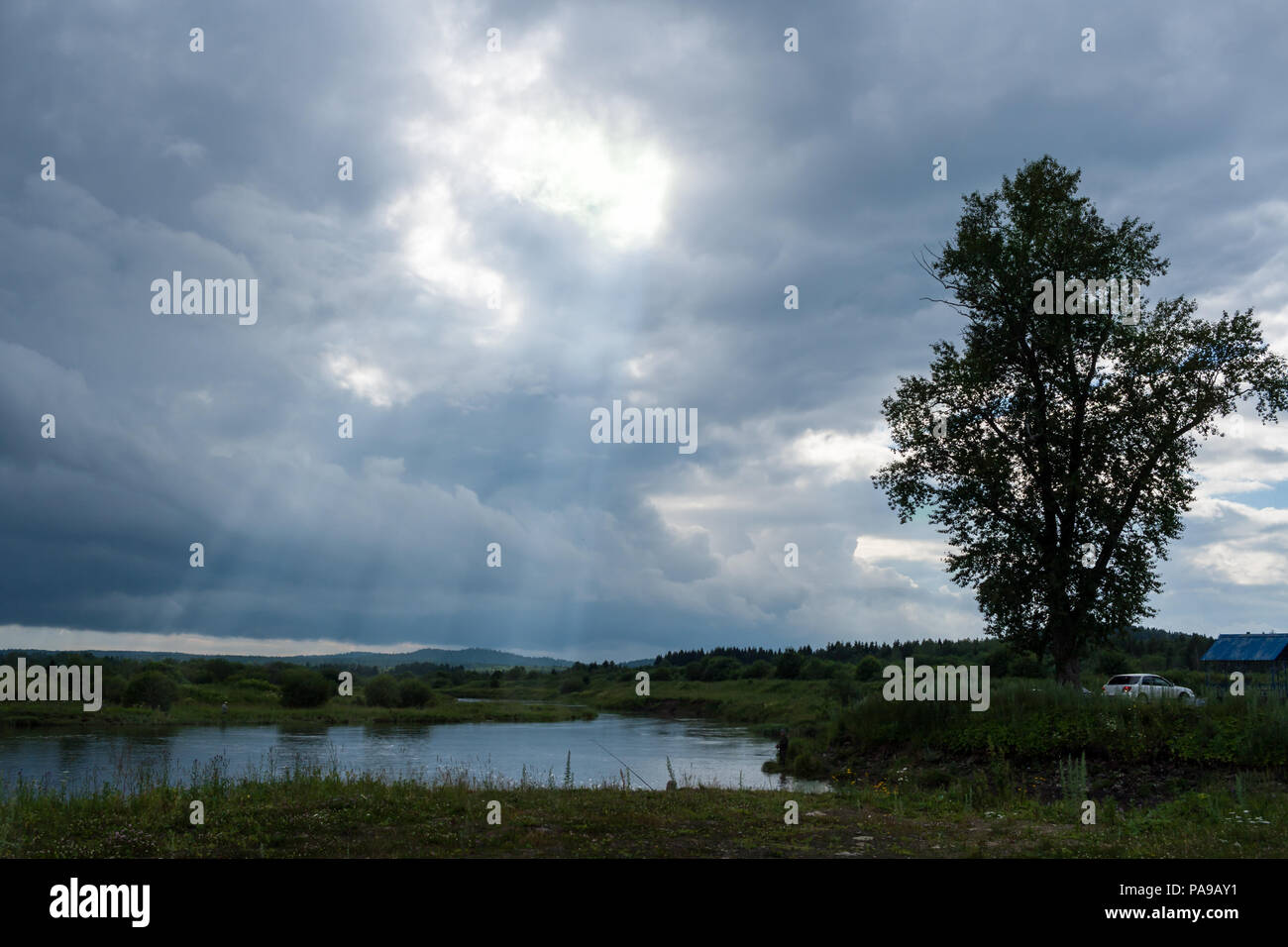 Small lake, fishermens and cloudy sky with sun rays. Stock Photo