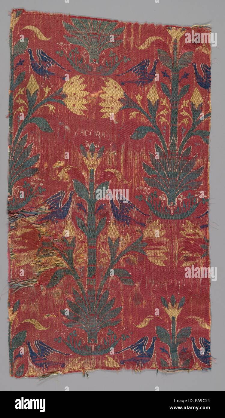 Fragment. Dimensions: Textile: H. 15 7/8 in. (40.3 cm)  W. 8 1/2 in. (21.6 cm). Date: 15th century.  This rectangular silk textile fragment displays a repetitive pattern of small flowers and plants in green, yellow, white, and blue in offset rows on a red ground. From the base of each plant spring small leaves and stems. Above each base, a lotus-like yellow flower with green buds and leaves rises from a palmette. Confronted long-necked birds with raised wings flank the stock.  This textile fragment is ornamented with a pattern of confronting long-necked birds perched on flower stalks, facing a Stock Photo