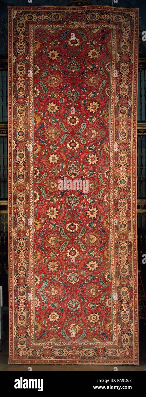 Carpet. Dimensions: Rug: L. 363 1/2 in (923.3 cm)  W. 133 1/2 in. (339.1 cm)  Wt. 186 lbs. (84.4 kg)  Storage Tube: L. 156 in. (396.2 cm)  Diam. 11 in. (27.9 cm). Date: mid-17th century.  The characteristic red of Indian carpets emphasizes the graceful yet dynamic design of the trellis pattern connecting the floral and serrated motifs. The serrated leaves enclosing a palmette, as well as the medallions and cartouches in the border, recall sixteenth century Herat carpets from Iran, but the exuberance of the floral forms and richness of color confirm an Indian origin. Museum: Metropolitan Museum Stock Photo