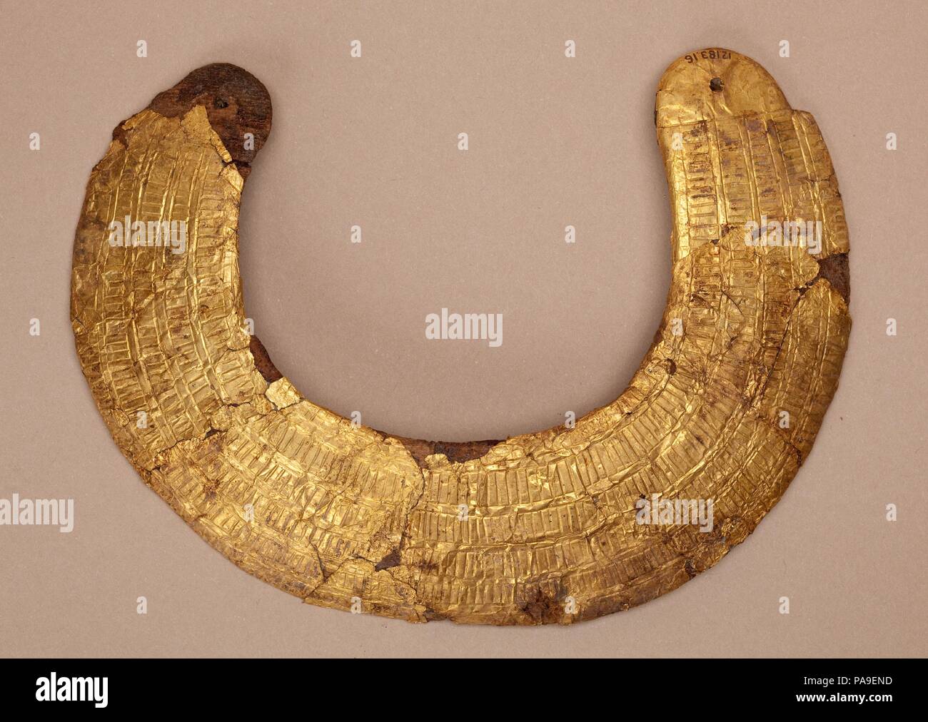 Model collar of Hapiankhtifi. Dimensions: W. 17 × Th. 1.5 cm (6 11/16 × 9/16 in.). Dynasty: Dynasty 12. Date: ca. 1981-1802 B.C..  Elaborate broad collars were worn by the Egyptian elite for a variety of festival and religious occasions. These could be floral, made from actual plant material, or crafted from individual elements of faience, metal, or semi-precious stone. This model collar of wood, gilded and engraved with representations of small beads in rows, echoing an actual example, was found on the chest of Hapiankhtifi's mummy. A string would have been passed through the holes in the two Stock Photo