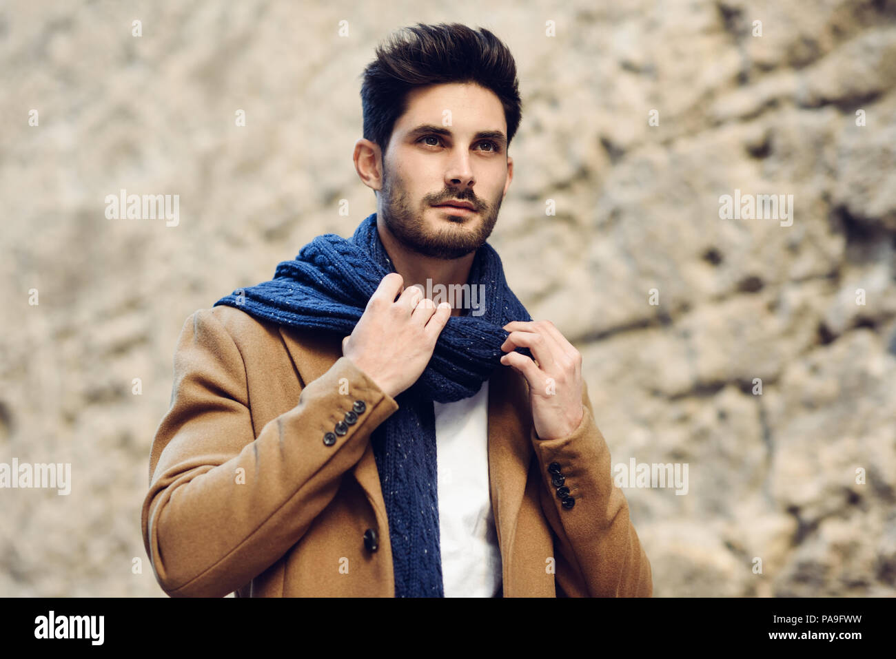 Young man wearing winter clothes in the street. Young bearded guy with  modern hairstyle with coat, scarf, blue jeans and t-shirt Stock Photo -  Alamy