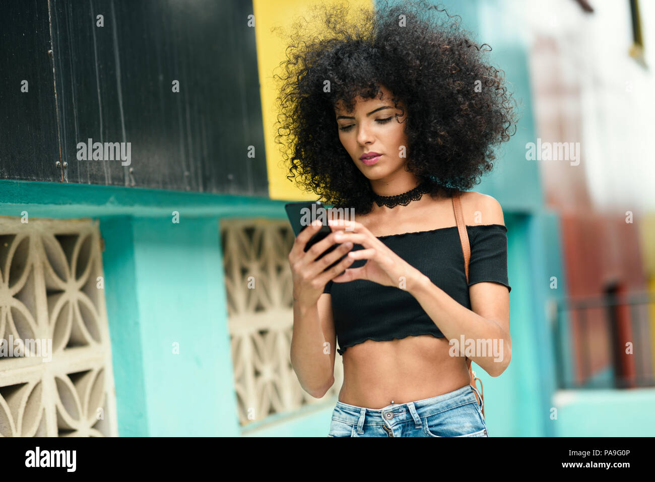 Young black woman with afro hair walking on the street holding a smart ...