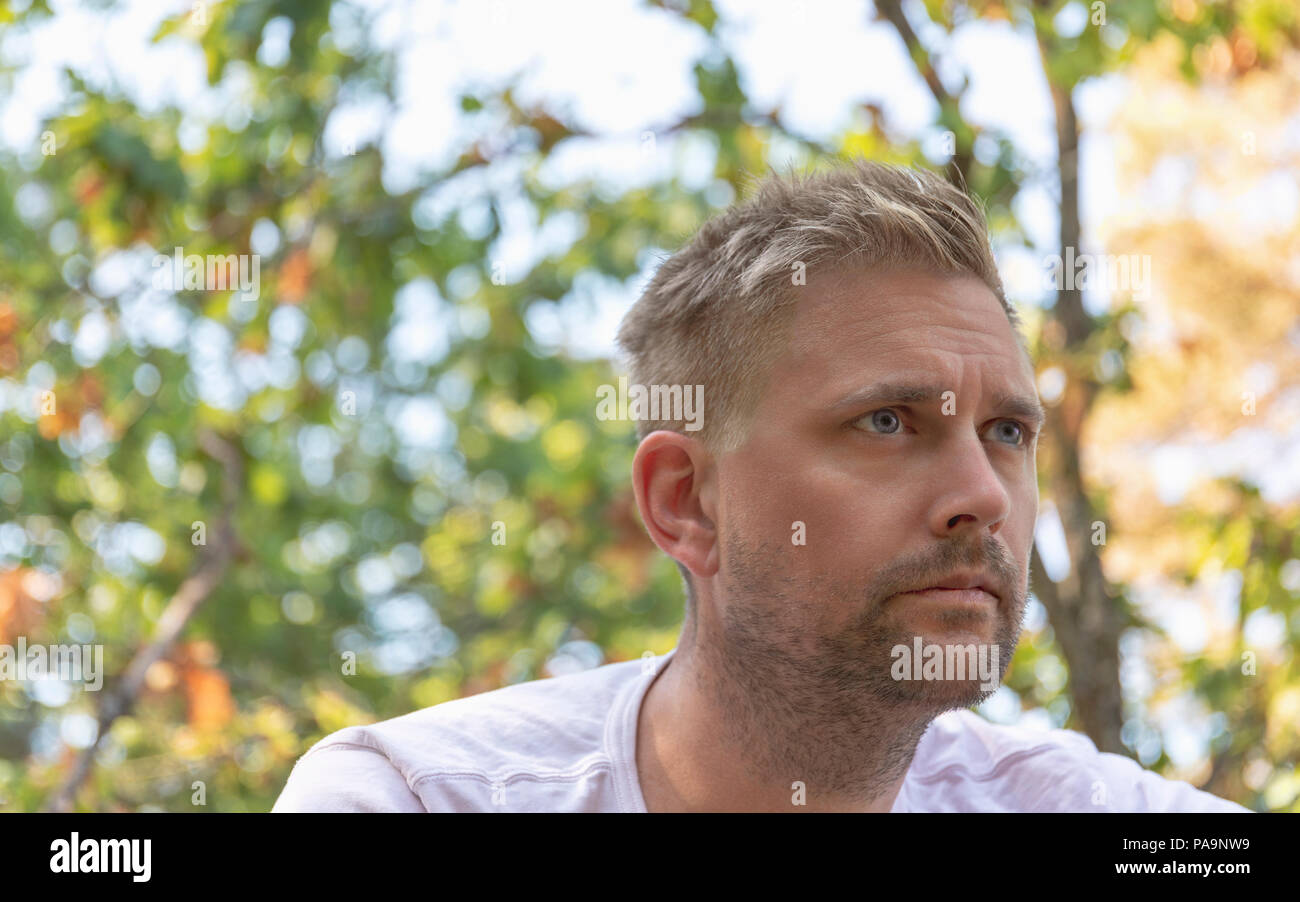 Handsome sexy blonde hair caucasian adult man looking away with look of determination and deep in thought outdoor portrait Stock Photo