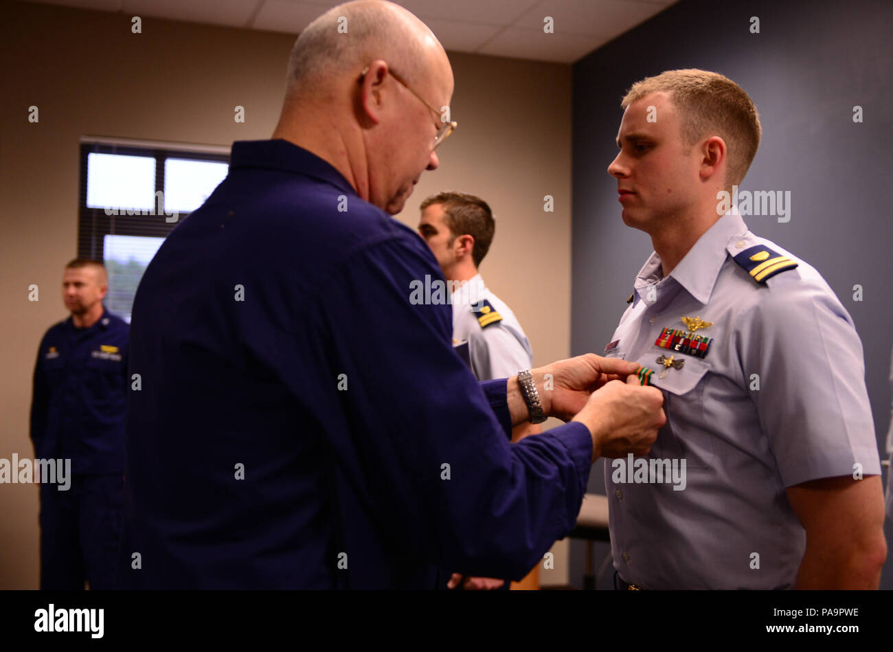 Rear Adm. Richard Gromlich, commander Coast Guard 13th District, presents Lt. Wesley Jones, an MH-65 Dolphin helicopter pilot at Coast Guard Air Station North Bend, Ore., with a Coast Guard Achievement Medal during an awards ceremony at Sector North Bend, March, 1, 2016. Jones was the co-pilot aboard a rescue helicopter during a rescue operation, which led to the rescue of four fishermen from the fishing vessel Jamie K after it ran aground near Cape Blanco, Ore., in July 2015. (U.S. Coast Guard photo by Petty Officer 1st Class Levi Read) Stock Photo