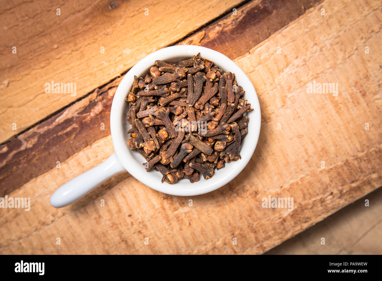 Exotic spices concept organic cloves in white cup on wood background