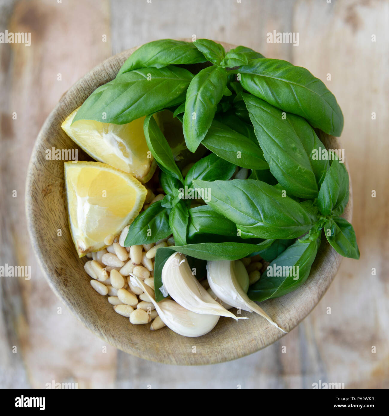 Flat lay bowl of pesto ingredients including fresh basil, lemons, garlic and pine nuts. Stock Photo