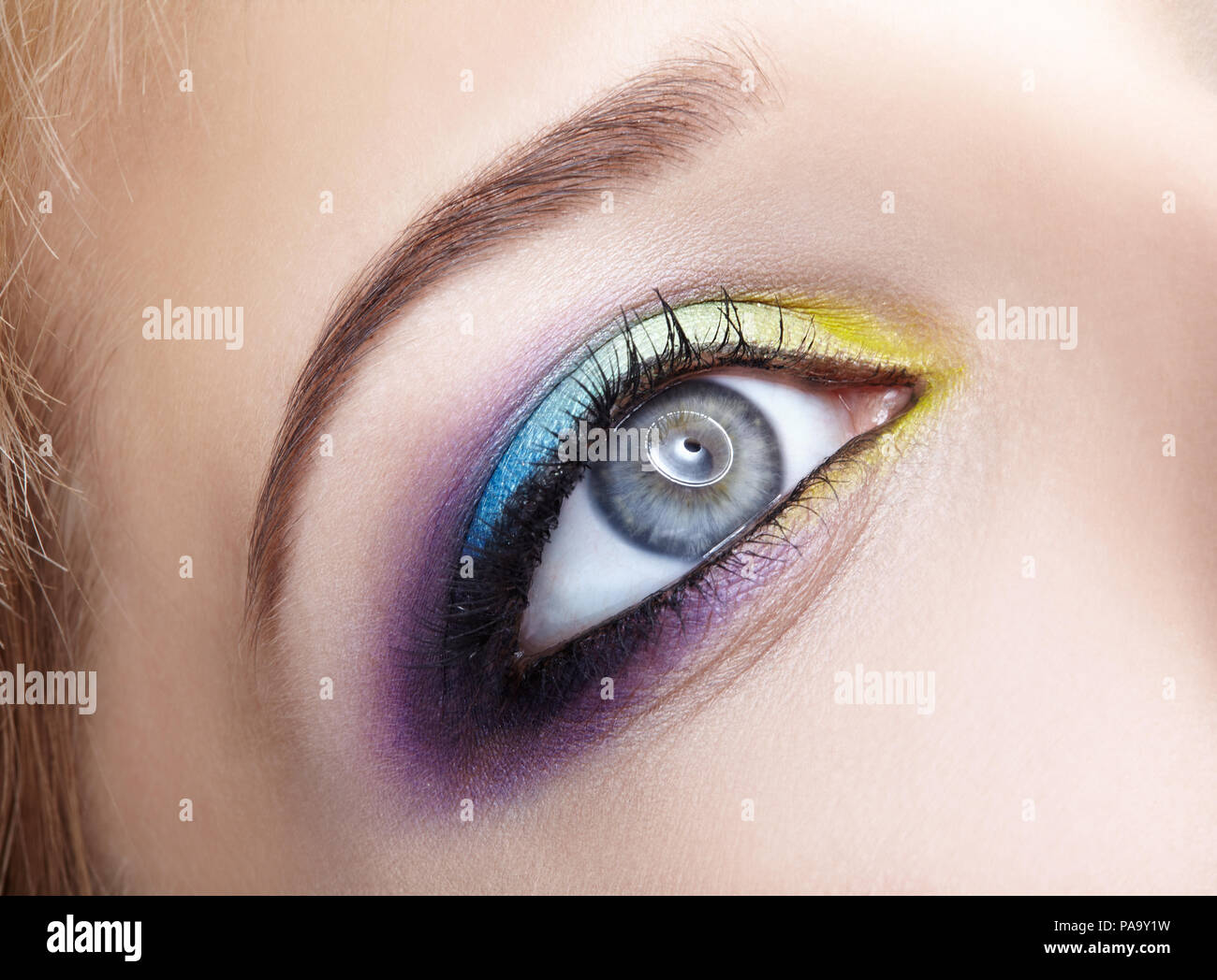 Closeup macro image of human female eye with violet shadows, blue and and yellow makeup Stock Photo