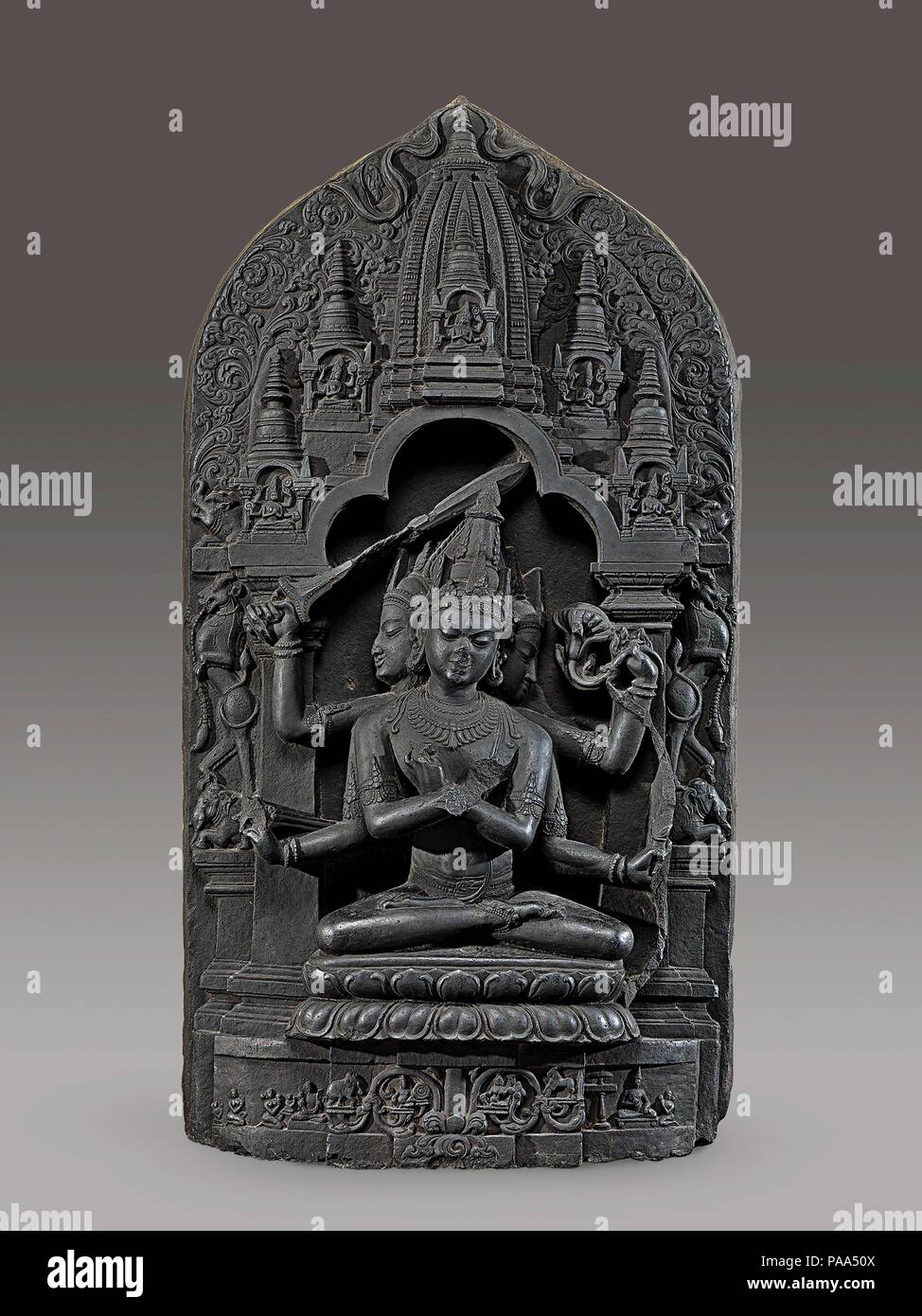 Manjuvajra Mandala. Culture: Bangladesh or India (Bengal). Dimensions: H. 46 in. (116.8 cm); W. 24 in. (61 cm); D. 7 1/2 in. (19.1 cm). Date: 11th century.  This sculpture represents an esoteric form of Manjushri, the Bodhisattva of Transcendent Wisdom. He has three heads and six arms; four hold a bow and arrow, a sword, and a lotus, while the remaining two hold vajras (thunderbolt scepters) and are crossed at the chest in an esoteric gesture (mudra) identifying supreme wisdom. Most prominent among this array of weapons is the sword, which cuts away ignorance and delusion. Leogryphs standing o Stock Photo