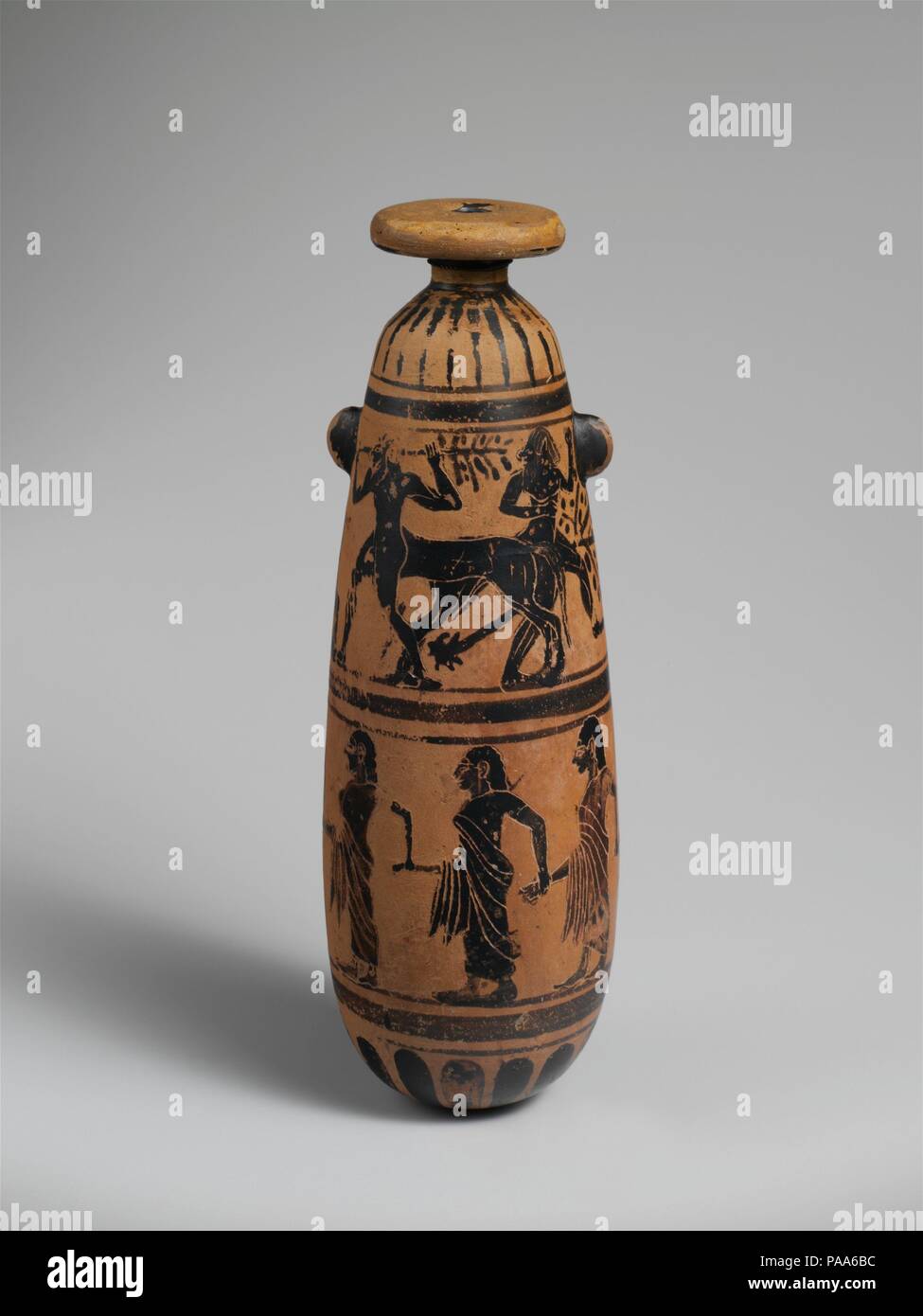 Terracotta alabastron (perfume vase). Culture: Etruscan. Dimensions: H. 7 1/8 in. (18.1 cm). Date: 6th century B.C..  Upper frieze, Herakles and centaurs  Lower frieze, flutist leading procession of women  The upper frieze, depicting Herakles in the company of three centaurs, is perhaps a reference to the story of the Greek hero's battle with Pholos and his fellow centaurs. The scene below has no obvious narrative connection to that one. This shape, frequently made of alabaster and copied by Corinthian potters, is rare with Etruscan potters working in Southern Etruria. Museum: Metropolitan Mus Stock Photo