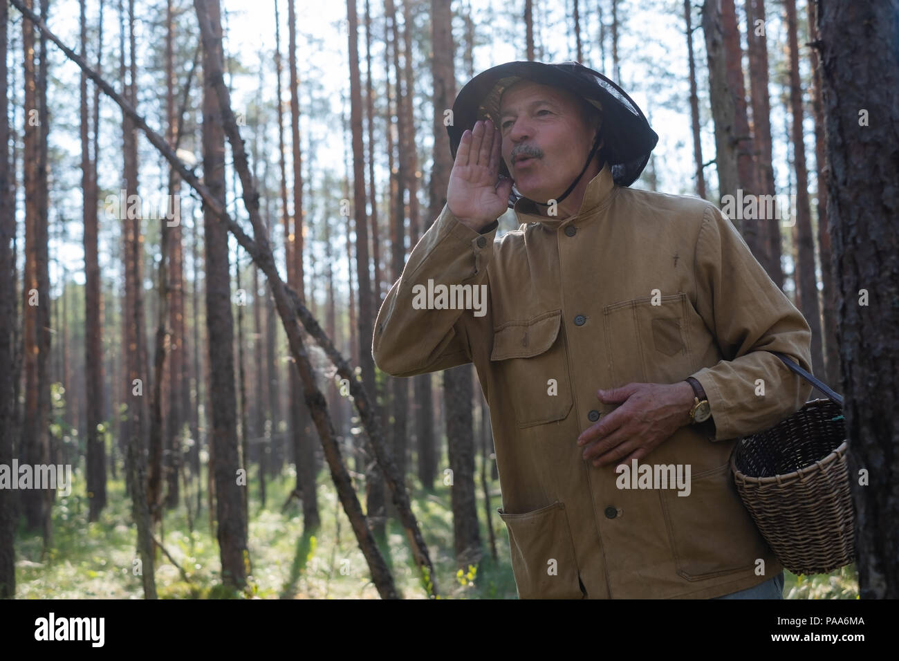 Where are you concept. Mature european man dressed in old clothes holding basket is lost in forest. He is shouting his friend trying to find him Stock Photo