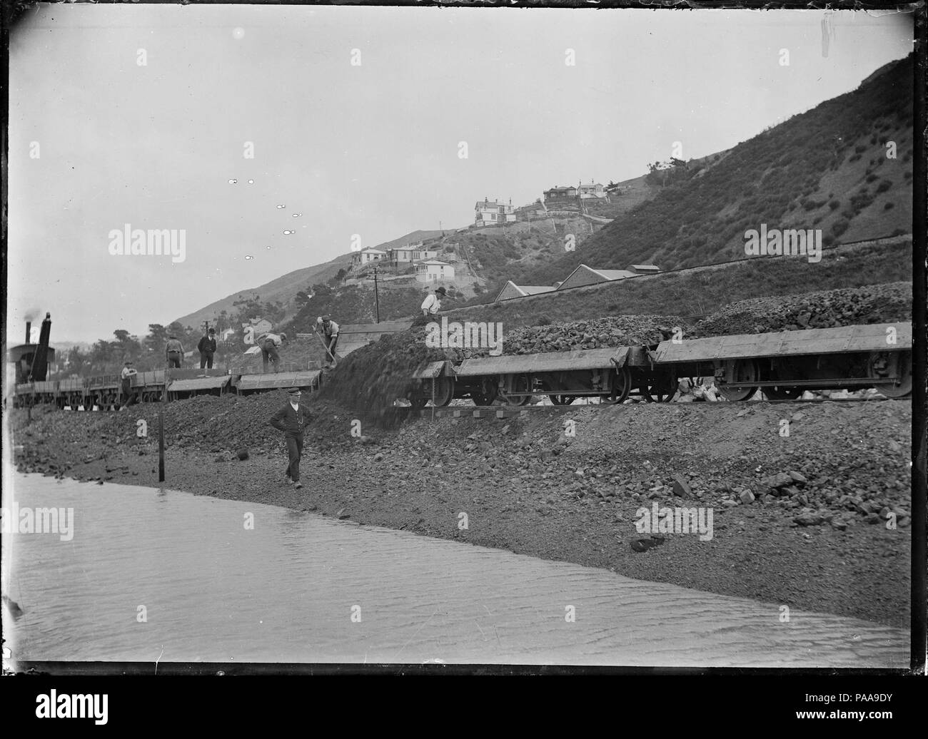 171 Men unloading spoil from railway trucks working with a ballast plough, on part of the reclamation at Kaiwharawhara, Wellington ATLIB 314480 Stock Photo