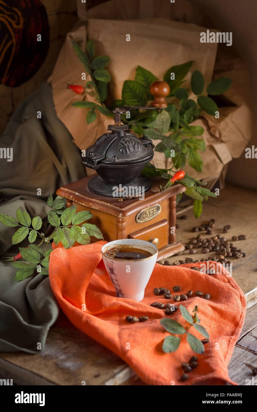 cup of coffee, a coffee grinder among the green leaves. Vintage style. Stock Photo