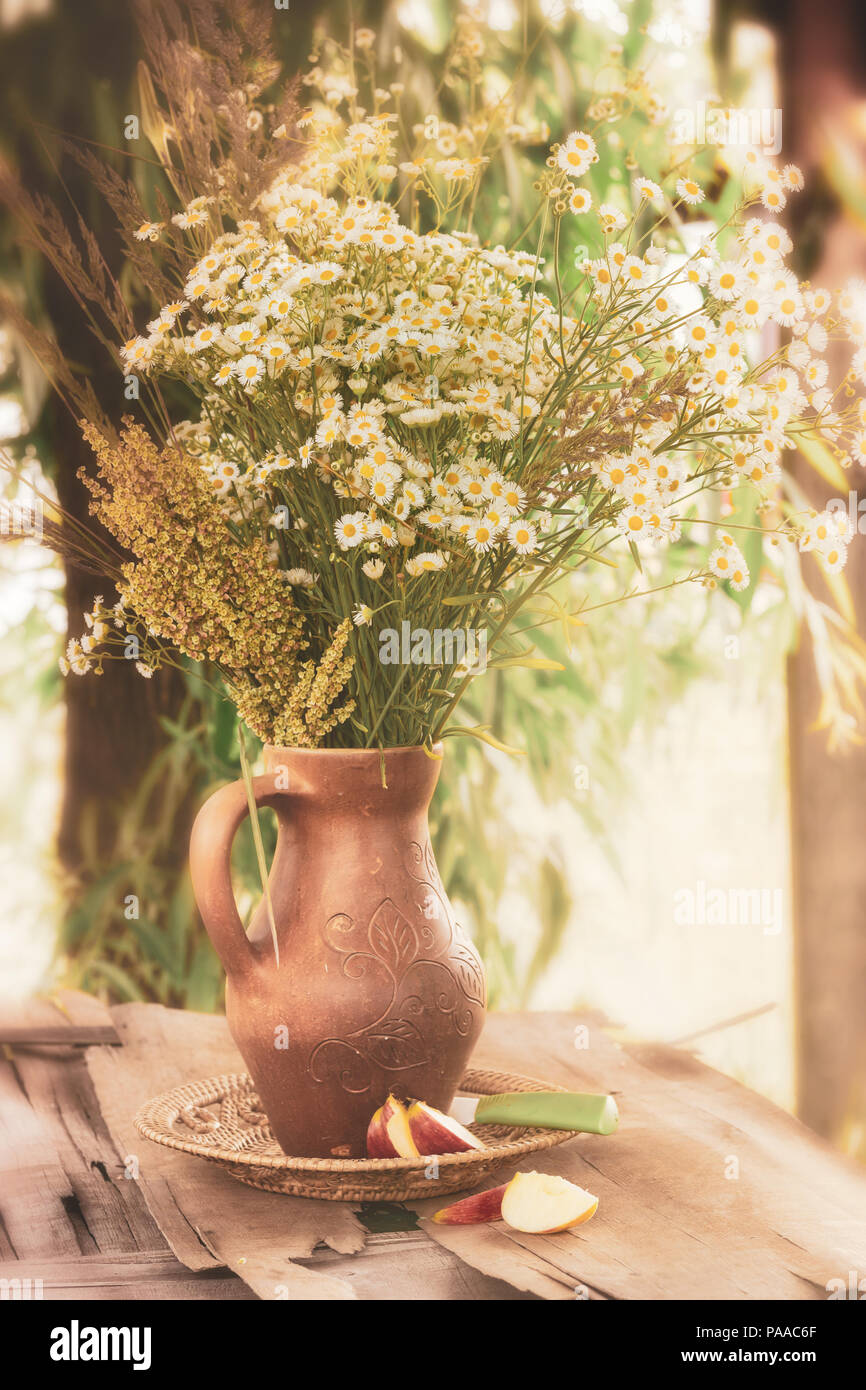 flowers with filter effect retro vintage style. Slow life.  A bouquet of chamomiles and wildflowers in a clay vase. Rural motive. Stock Photo
