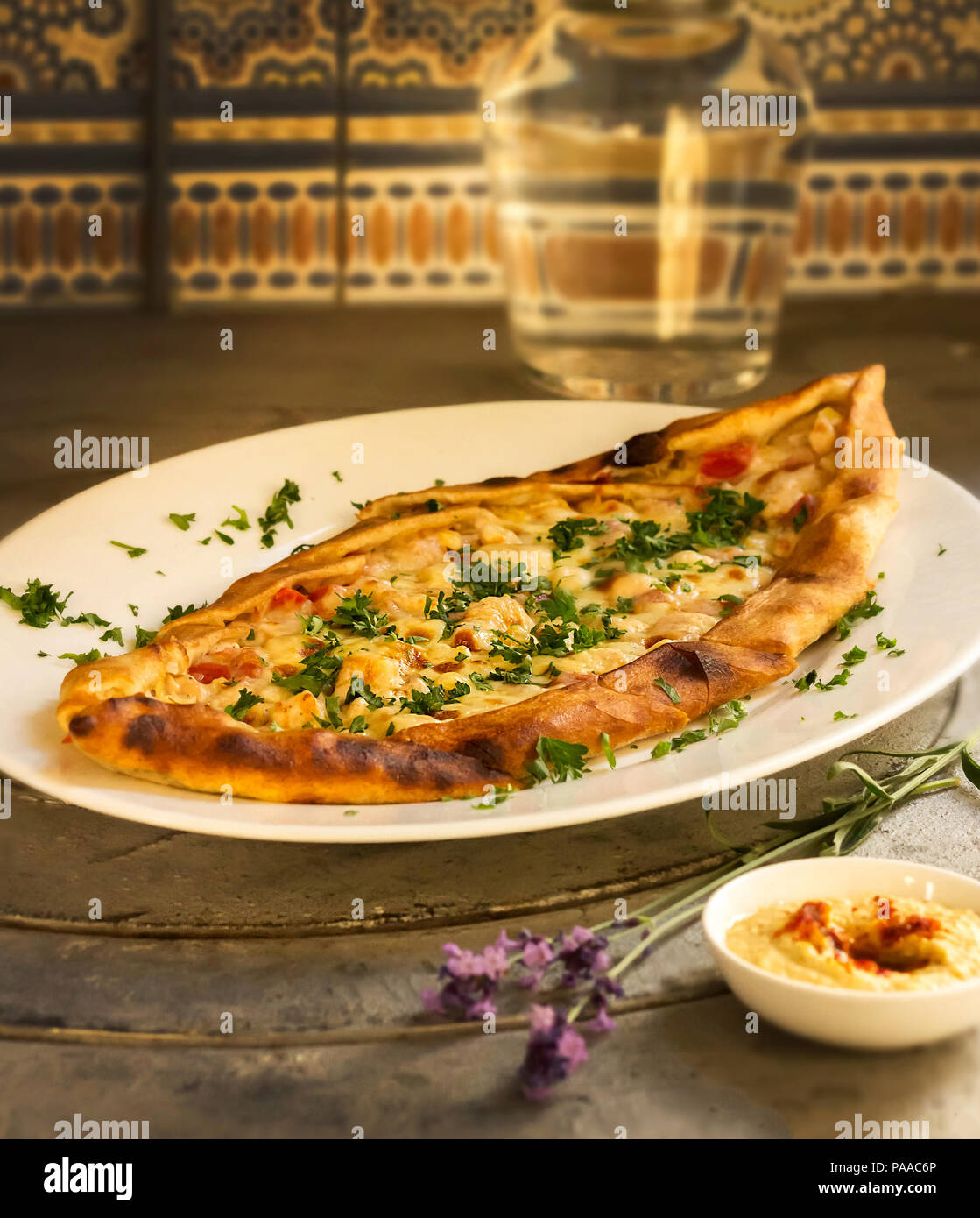 A hot pizza with chicken, cheese and greens lies on a plate. Next to the bowl with sauce and a branch of lavender Stock Photo