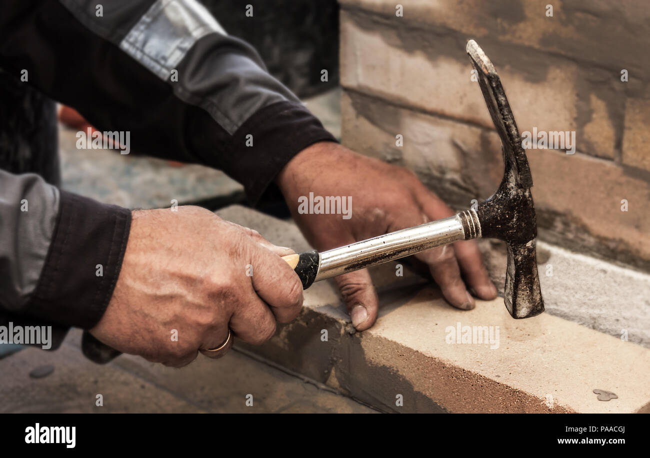 The builder's hands with a hammer and a brick Stock Photo