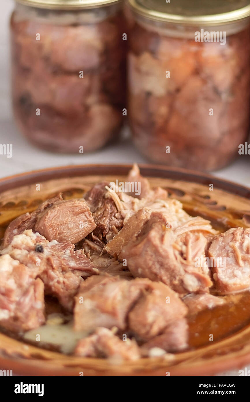 pieces of stew meat on a clay plate on the background of glass cans with home preservation. Home cooking Stock Photo