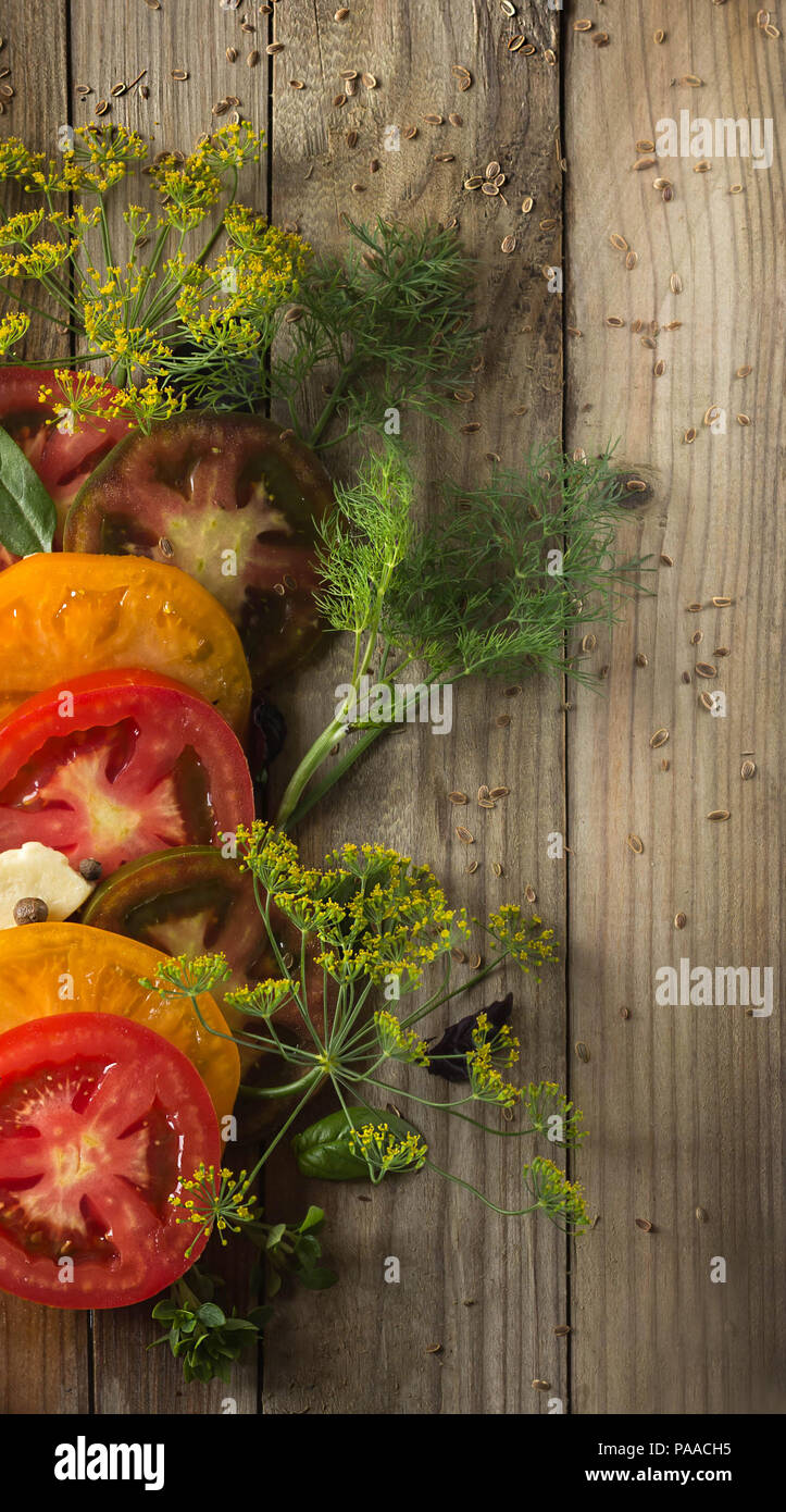 Ripe tomatoes, dill, basil leaves and a slice of cheese lie on gray boards. Around the seeds of dill scattered Stock Photo