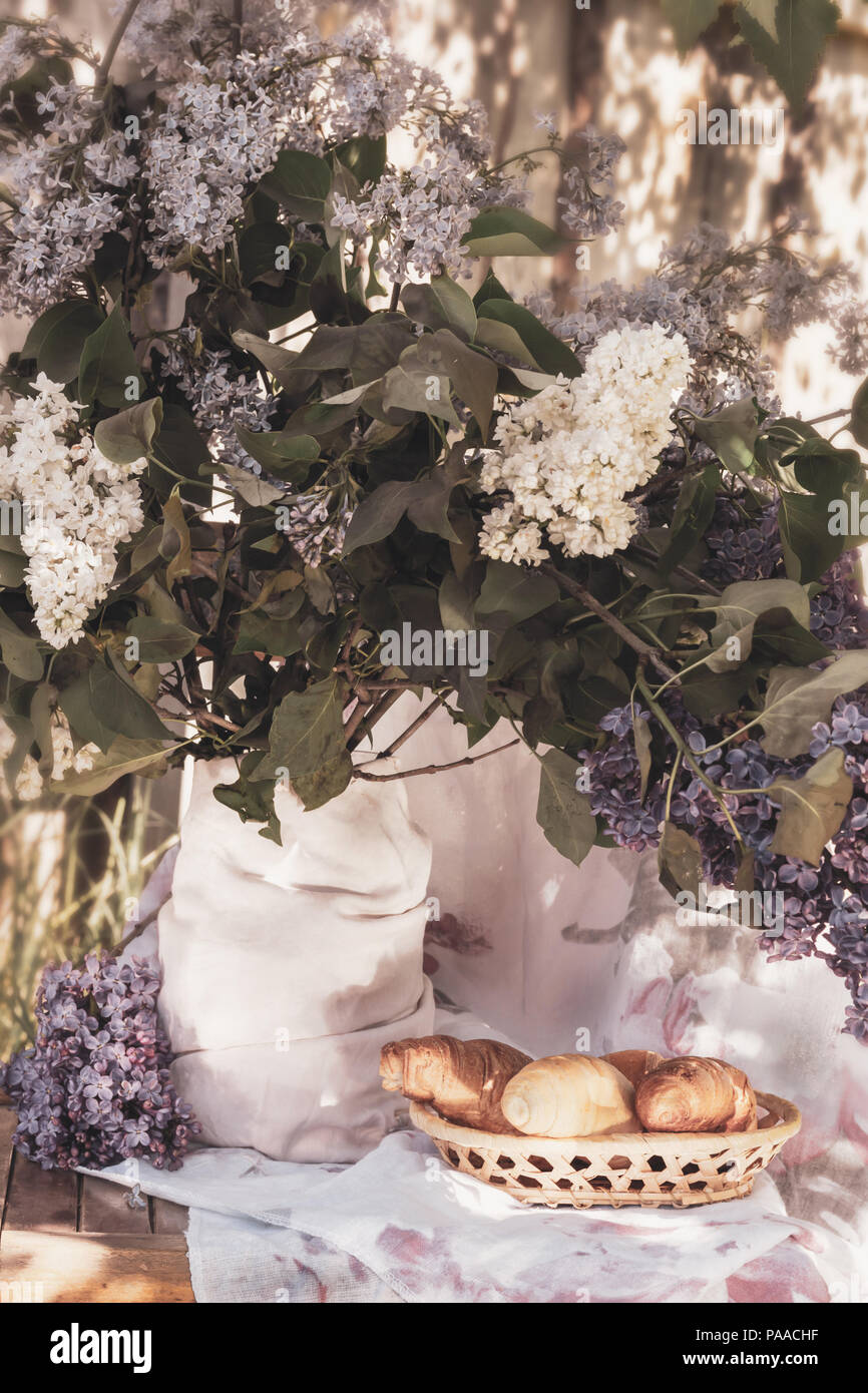 Croissants in a wicker basket on a background of lilac flowers Stock Photo