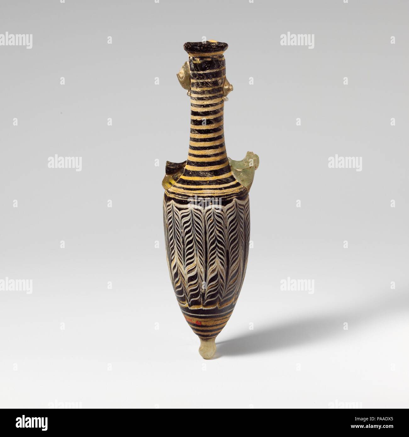Glass amphoriskos (perfume bottle). Culture: Greek, Eastern Mediterranean. Dimensions: H.: 7 1/16 in. (17.9 cm). Date: 2nd to mid-1st century B.C..  Translucent cobalt blue; handles and base-knob in translucent colorless with pale green tinge, but one handle with additional trail in dark olive green, appearing black; trails in opaque white and opaque yellow .  Uneven rim-disk, with rounded edge and sloping inward; tall, slender cylindrical neck, with tooling indents around top; narrow sloping shoulder; elongated, narrow ovoid body; pointed bottom with applied base-knob; two vertical handles ap Stock Photo