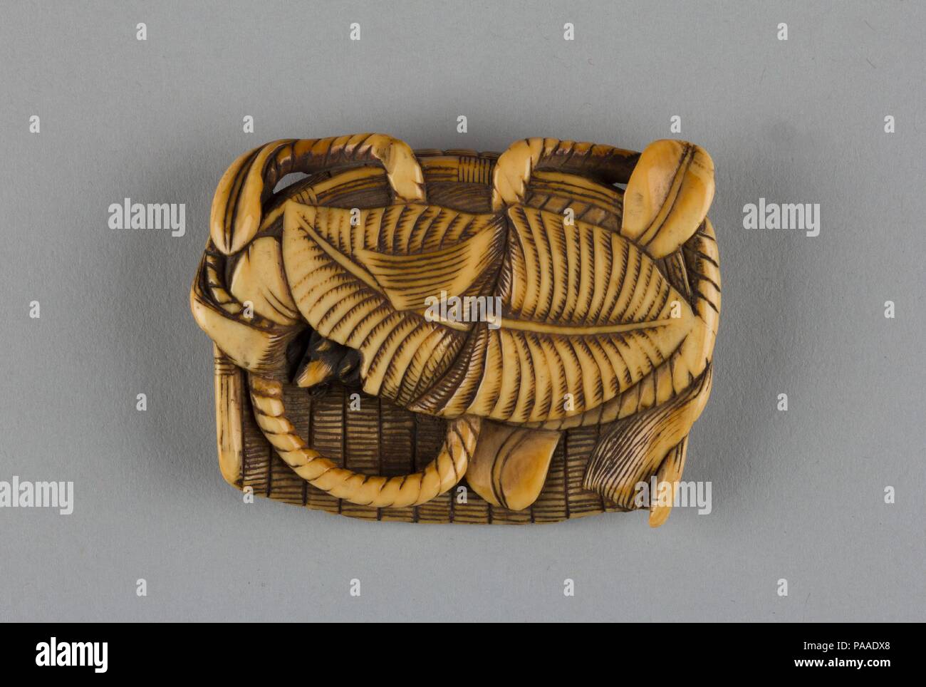 Netsuke of Flat Basket Containing Leaves and a Mouse. Culture: Japan. Dimensions: H. 3/4 in. (1.9 cm); W. 2 7/8 in. (7.3 cm); D. 2 in. (5.1 cm). Date: 19th century. Museum: Metropolitan Museum of Art, New York, USA. Stock Photo