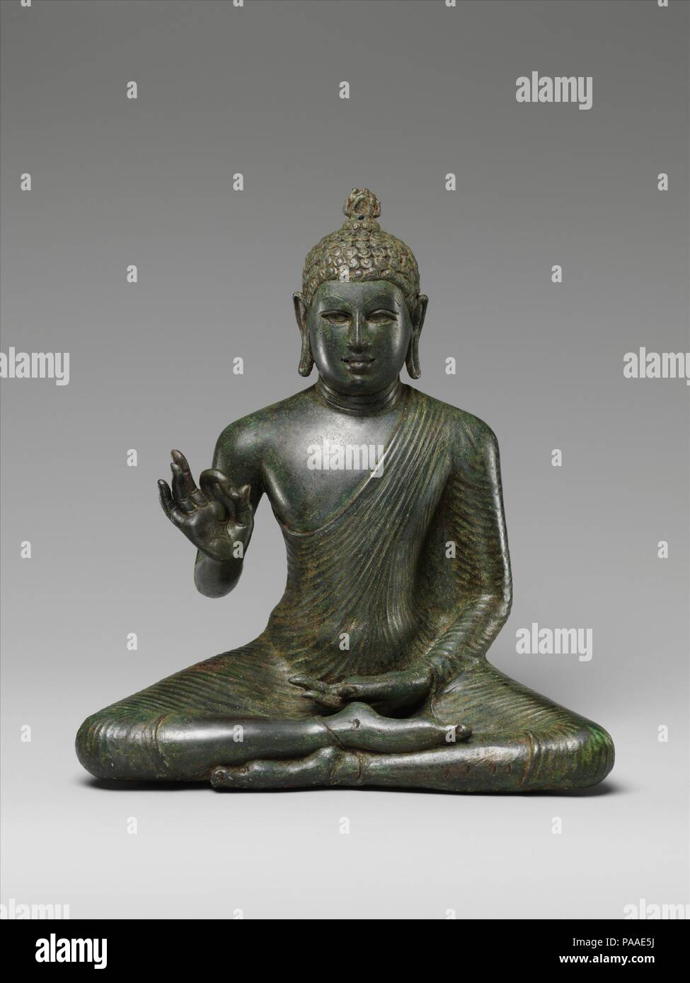 Buddha Expounding the Dharma. Culture: Sri Lanka (Anuradhapura). Dimensions: H. 10 1/2 in. (26.7 cm); W. 11 in. (7.9 cm); D. 4 1/2 in. (11.4 cm). Date: late 8th century.  The quintessential icon of early Buddhist Sri Lanka is the Buddha gesturing vitarka-mudra, imparting his dharma to all. Seated in a meditative yogic posture, he wears the monk's uttarasanga, an untailored length of cloth drawn tautly around the body, with his right shoulder exposed in the southern manner of Buddhism. His hair is expressed in short, tight curls to evoke his renunciation of the material world, when he cut off h Stock Photo