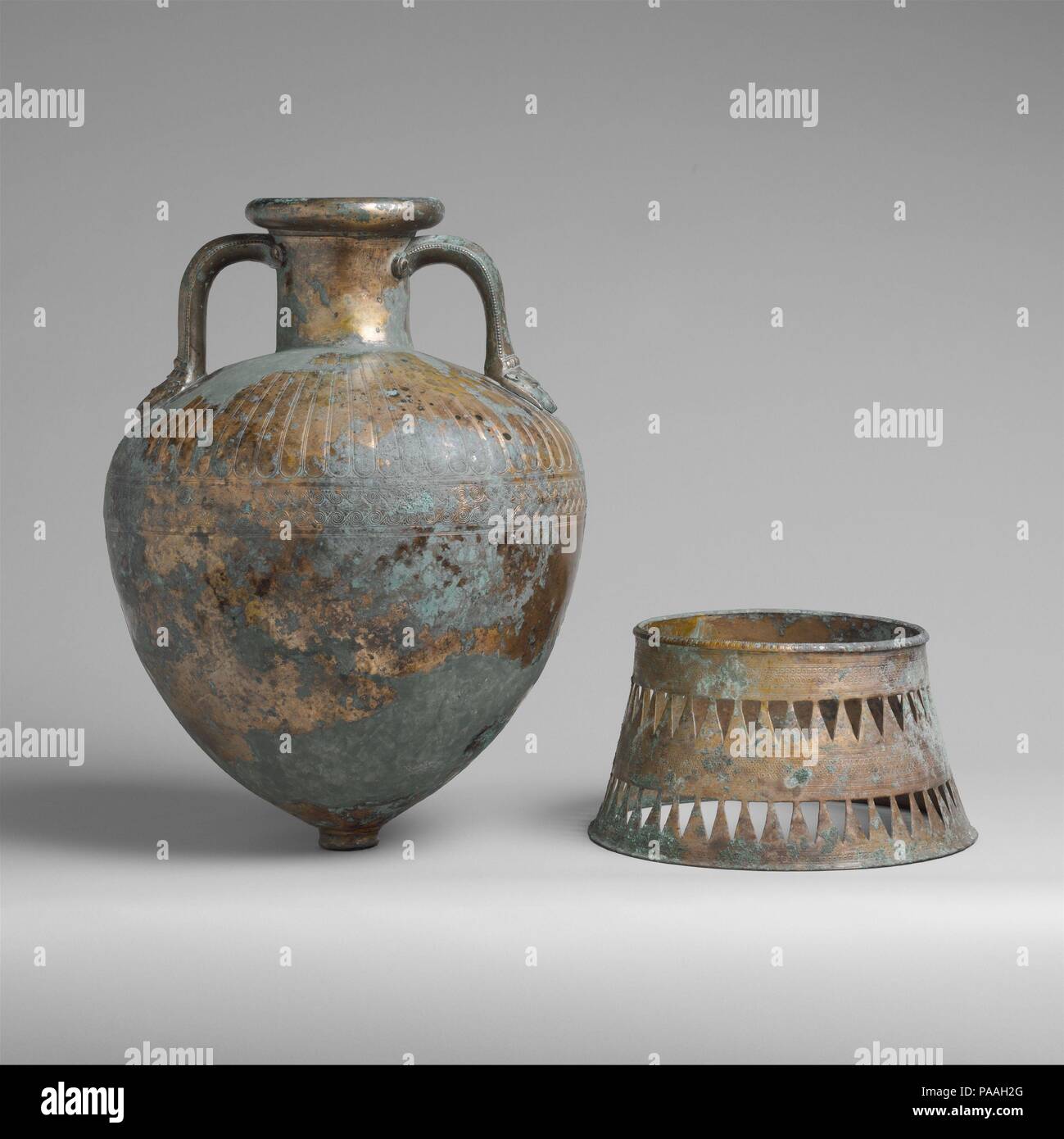 Bronze pointed neck-amphora with stand. Culture: Greek. Dimensions: Total H. of amphora on stand  22 3/4 in. (57.8 cm)  H. of amphora  19 in. (48.3 cm)  H. of stand  6 3/4 in. (17.1 cm). Date: ca. 500-450 B.C..  The gleaming golden color visible on the surface of these bronzes provides a rare glimpse of the original appearance of a bronze from classical antiquity.  The quality of the chasing on the amphora is particularly fine; on the shoulder is a tongue pattern in shallow relief, below which are bands and running spirals with a chain of horizontal palmettes in between.  The separately cast h Stock Photo