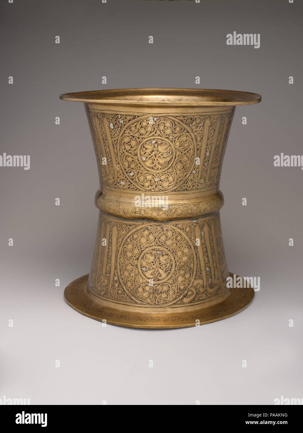 Tray Stand. Dimensions: H. 9 9/16 in. (24.3 cm)  Diam. (Rim) 9 3/16 in. (23.3 cm). Date: 14th century.  This tray stand exemplifies the work produced for highranking Mamluk patrons. The inscription's honorifics indicate that its owner was a governor under Sultan al-Nasir Muhammad (1310-41), during whose reign human and animal imagery lost favor, even on objects for secular use. A few groupings of small ducks are the only creatures depicted. Note on the central band and upper rim the inclusion of six-petalled rosettes, an emblem sometimes used by this sultan and his amirs. Museum: Metropolitan  Stock Photo