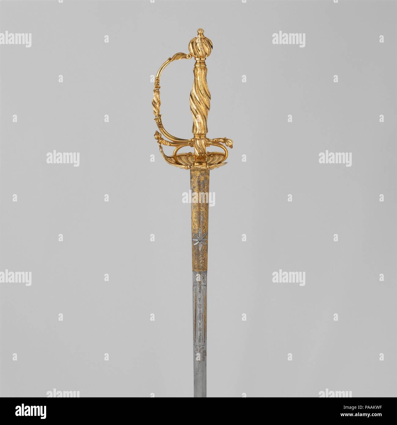 Smallsword. Culture: German or Dutch. Dimensions: L. 36 3/8 in. (92.5 cm); L. of blade 30 3/4 in. (78.2 cm); W. 3 1/4 in. (8.3 cm); D. 3 7/16 in. (8.7 cm); Wt. 1 lb. 0.4 oz. (464.9 cm). Date: ca. 1750-60.  The spirally channeled surfaces and elegant foliate finials on the guards typify the flamboyant Rococo style. The small proportions suggest the sword was made for a young man. Although not hallmarked, this exquisitely detailed gold hilt is probably of either German or Dutch manufacture. Museum: Metropolitan Museum of Art, New York, USA. Stock Photo