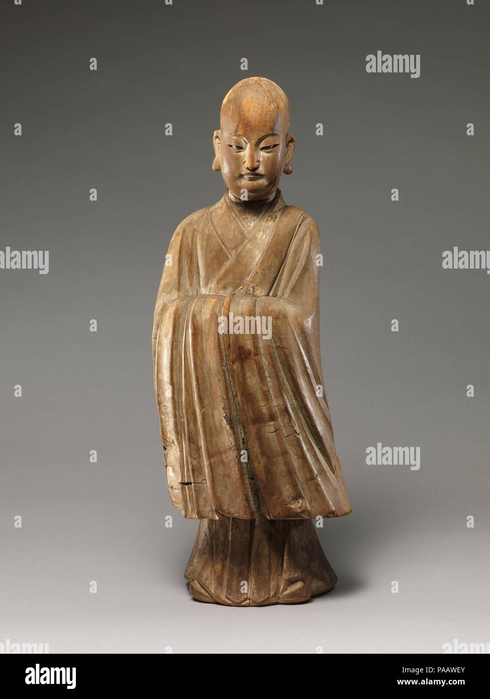 Arhat (Luohan). Culture: China. Dimensions: H. 19 1/8 in. (48.6 cm); W. 7 in. (17.8 cm). Date: 16th-17th century.  This sculpture epitomizes the merging of religious and secular imagery in later Chinese Buddhist sculpture. With his shaven head and elongated earlobes, the figure resembles a luohan (one of the Indian disciples of the Buddha), but his refined facial features, dignified posture, long-sleeved robe, and pointed shoes--all attributes associated with Confucian scholar-officials--identify him unmistakably as a youthful monk.  The sculpture's tendency toward abstraction and stylization- Stock Photo