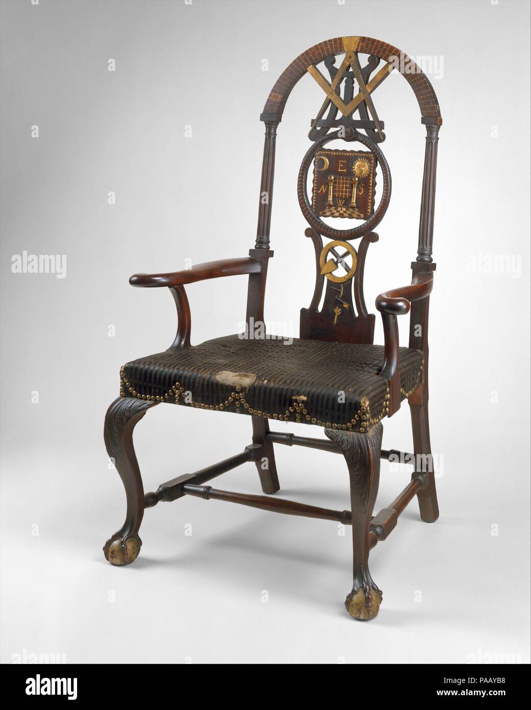 Masonic Armchair. Culture: American. Dimensions: 50 1/2 x 25 5/8 x 24 3/4 in. (128.3 x 65.1 x 62.9 cm). Date: 1775-90.  The seat and legs of this example are typical of the best Boston Rococo chairs, but the back is unusual. It is made up of Masonic symbols: fluted columns (referring to King Solomon's temple), a rusticated arch (arch of heaven), a compass and square (faith and reason), a mason's level (equality), a serpent swallowing its tail (rebirth), and a trowel (cement of brotherly love). The chair was probably made for the senior warden of an as-yet-unidentified Massachusetts lodge. Muse Stock Photo