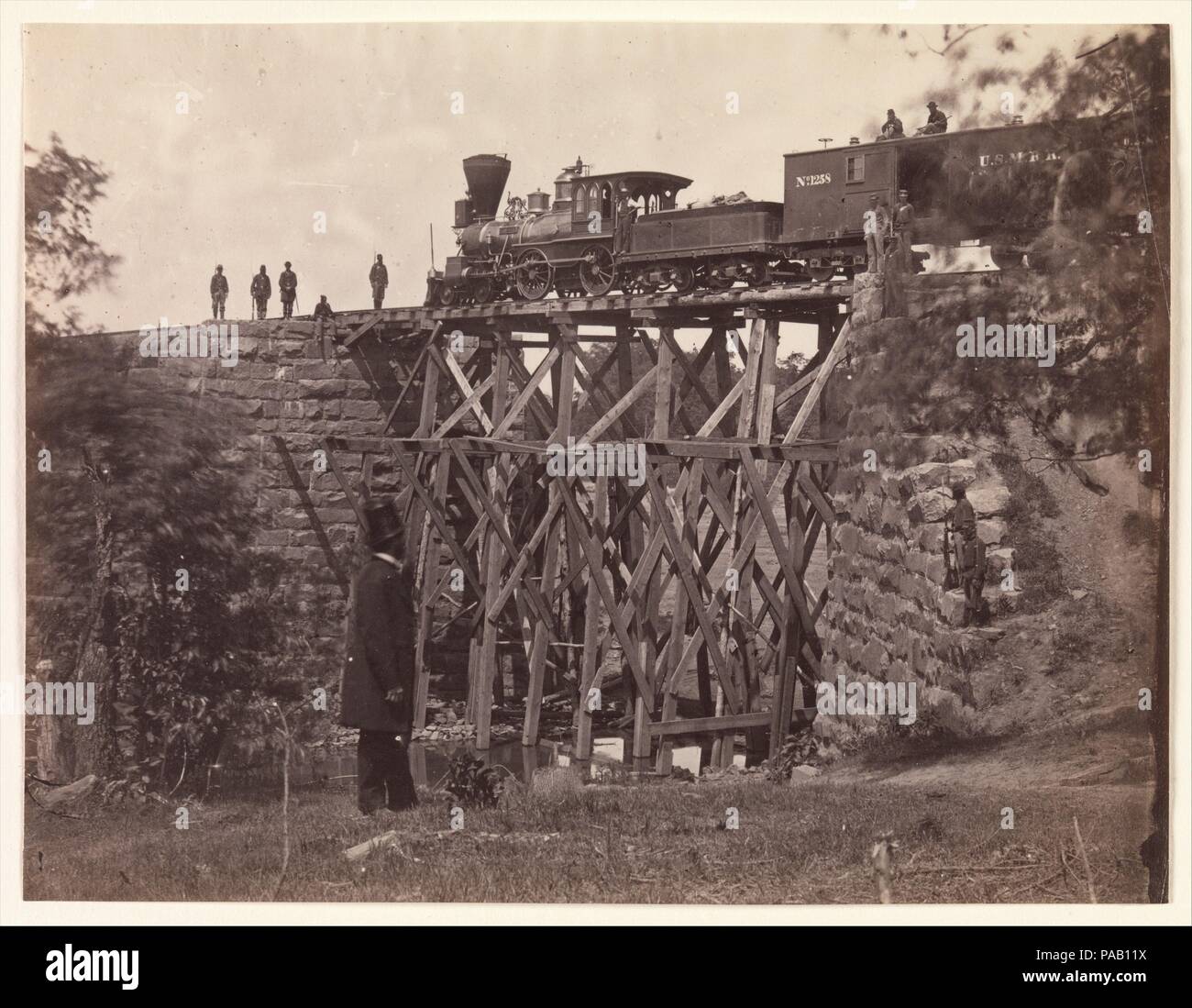 Bridge on Orange and Alexandria Rail Road, as Repaired by Army Engineers under Colonel Herman Haupt. Artist: Andrew Joseph Russell (American, 1830-1902). Former Attribution: Formerly attributed to Mathew B. Brady (American, born Ireland, 1823?-1896 New York). Date: 1865.  This view by Russell documents the engine Fire Fly testing the stability of a new wooden trestle bridge built quickly by the United States Military Railroad engineers to replace a masonry bridge destroyed by the Confederates. Atop the box car trailing the engine is a pair of armed sentries; others are on the rail tracks and b Stock Photo