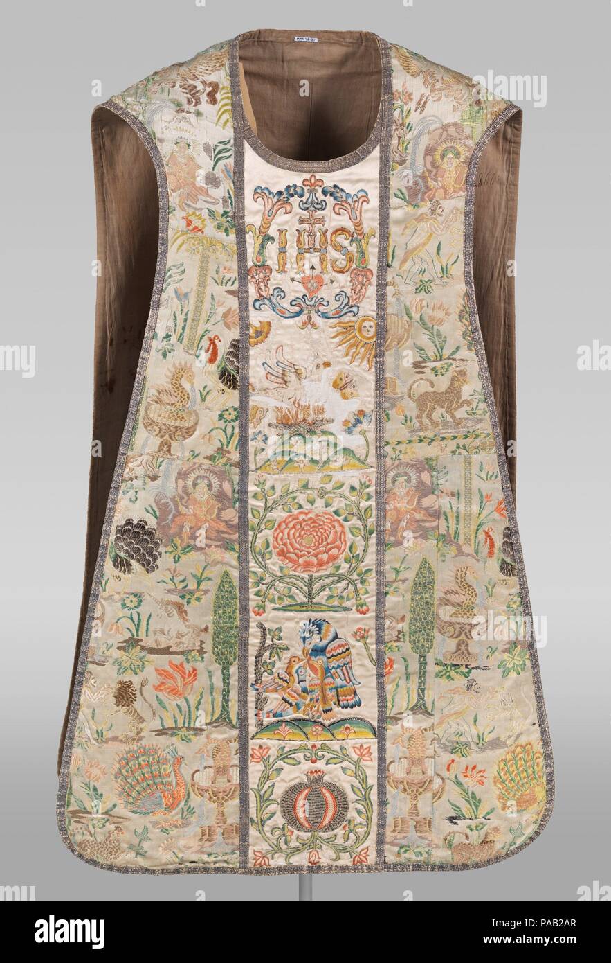 Chasuble. Culture: Portuguese. Dimensions: 48 × 29 in. (121.9 × 73.7 cm). Date: early 18th century.  This extravagant chasuble was likely constructed and used in Portugal. A variety of secular (fountains, peacocks, leopards, and turkeys) and mythical (unicorns, Hercules fighting a lion) images are scattered throughout the brocaded side panels, in contrast with the center panels, which are embroidered with traditional Christian motifs.  The materials may have been sourced in Asia and Europe. The woven body fabric is Portuguese while the white satin ground of the center panels is embroidered wit Stock Photo