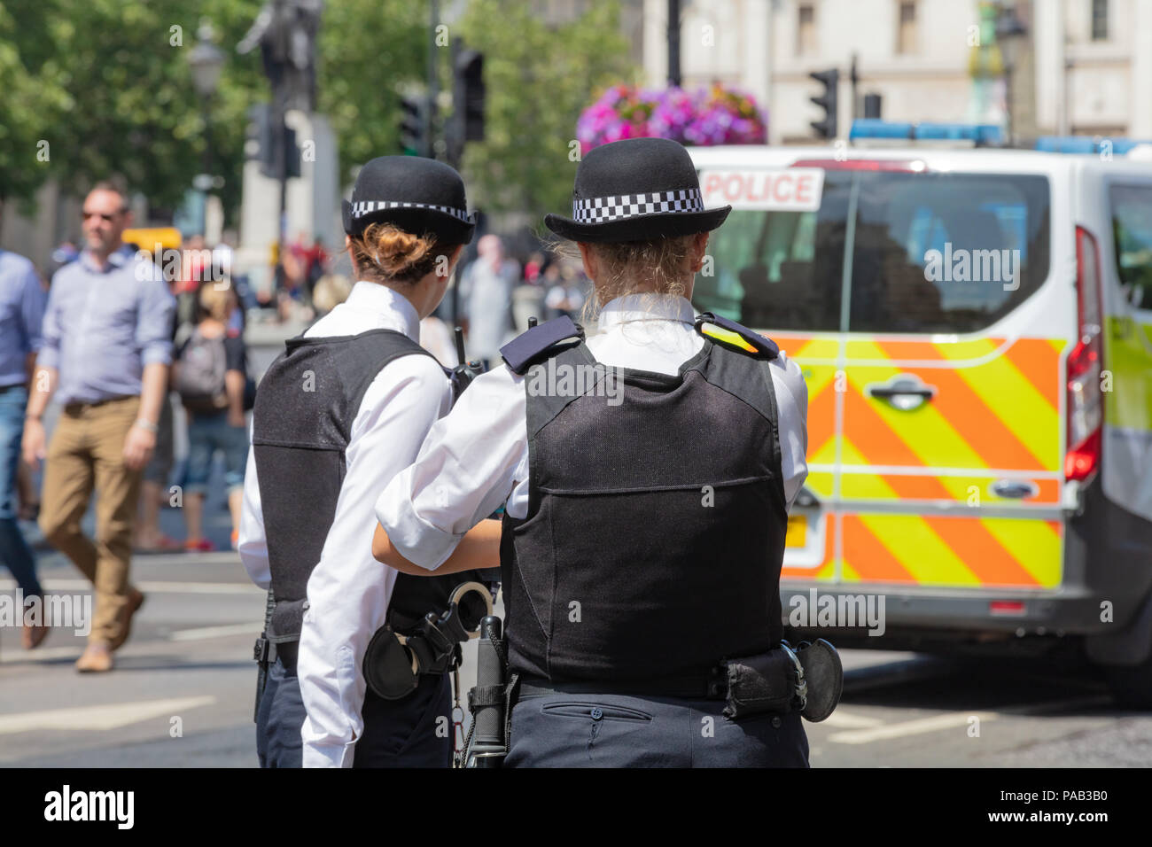 London, England, UK; 13th July 2018; Rear view of Two Female Metropolitan Police Officers in the Street.  Unfocused Police Van Behind Stock Photo