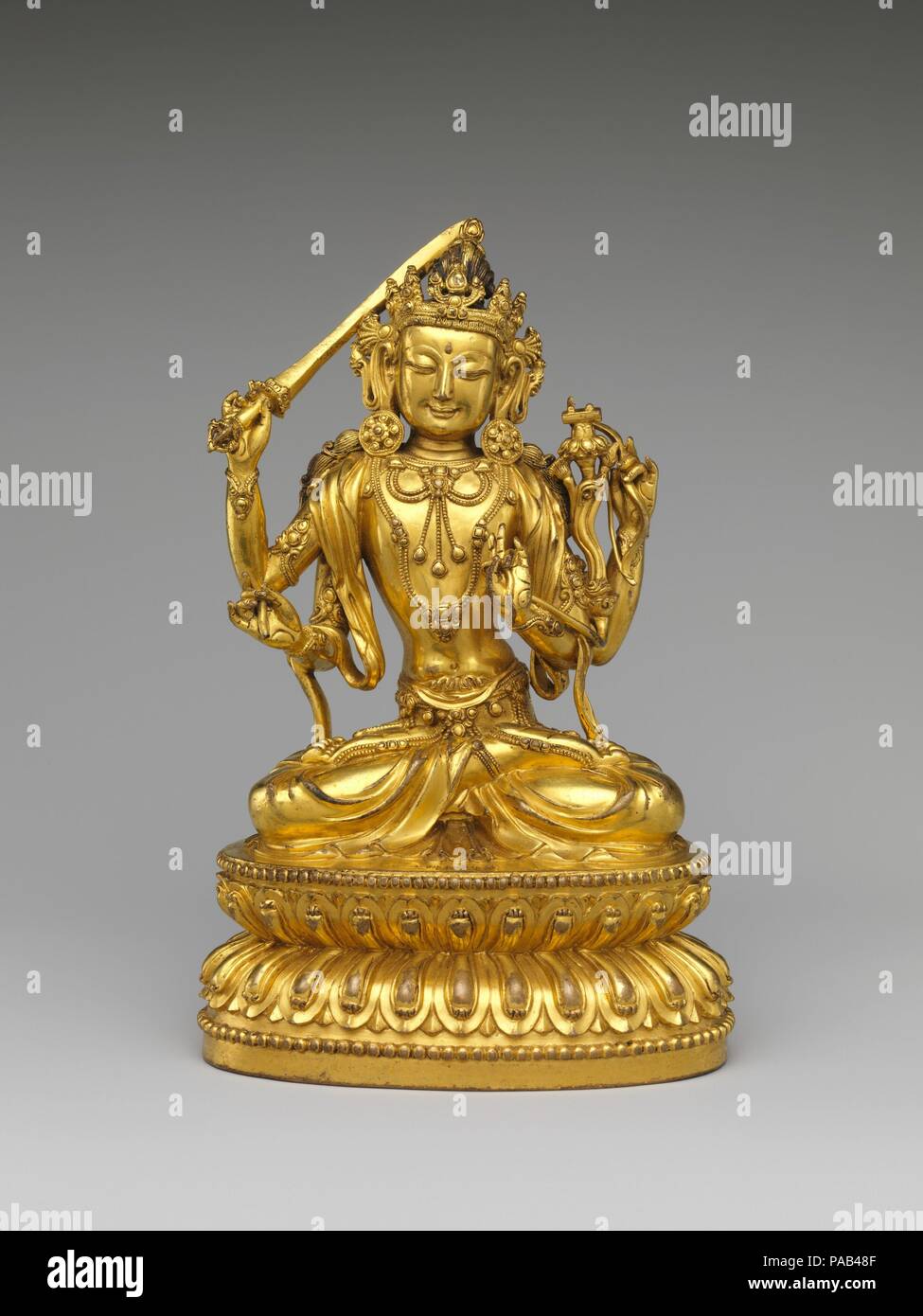 Bodhisattva Manjushri as Tikshna-Manjushri (Minjie Wenshu). Culture: China. Dimensions: H. 7 1/2 in. (19.1 cm); W. 4 3/4 in. (12.1 cm); D. 3 1/2 in. (8.9 cm).  Manjushri holds a sword in his primary right hand and a volume of the Perfection of Wisdom Sutra (which rests on a small lotus) in his left. Remnants of a bow and arrow can be seen in his secondary hands, and the combination of the four implements identify the sculpture as a Tikshna- Manjushri, a manifestation that refers to the bodhisattva's quick wit while further elucidating his position as an embodiment of spiritual wisdom.   The in Stock Photo