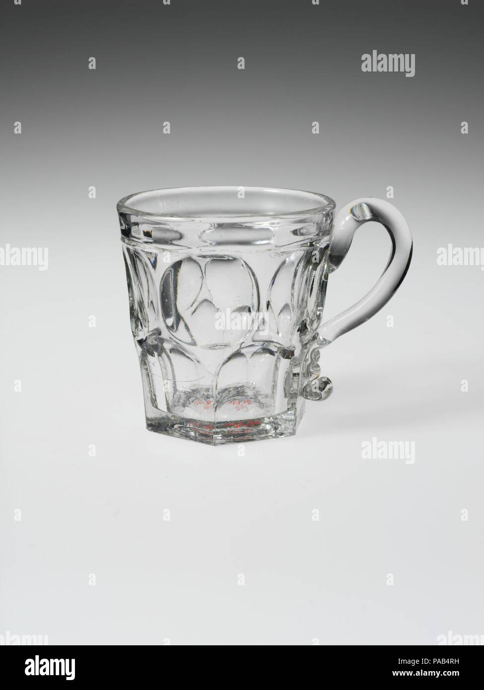 Mug. Culture: American. Dimensions: H. 3 7/8 in. (9.8 cm); Diam. 2 3/4 in. (7 cm). Date: 1830-70.  With the development of new formulas and techniques, glass-pressing technology had improved markedly by the late 1840s. By this time, pressed tablewares were being produced in large matching sets and innumerable forms. During the mid-1850s, colorless glass and simple geometric patterns dominated. Catering to the demand for moderately-priced dining wares, the glass industry in the United States expanded widely, and numerous factories supplied less expensive pressed glassware to the growing market. Stock Photo