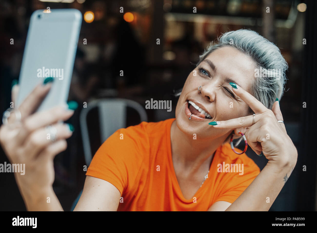 Attractive blonde woman making selfie at cafe and showing sign of victory Stock Photo