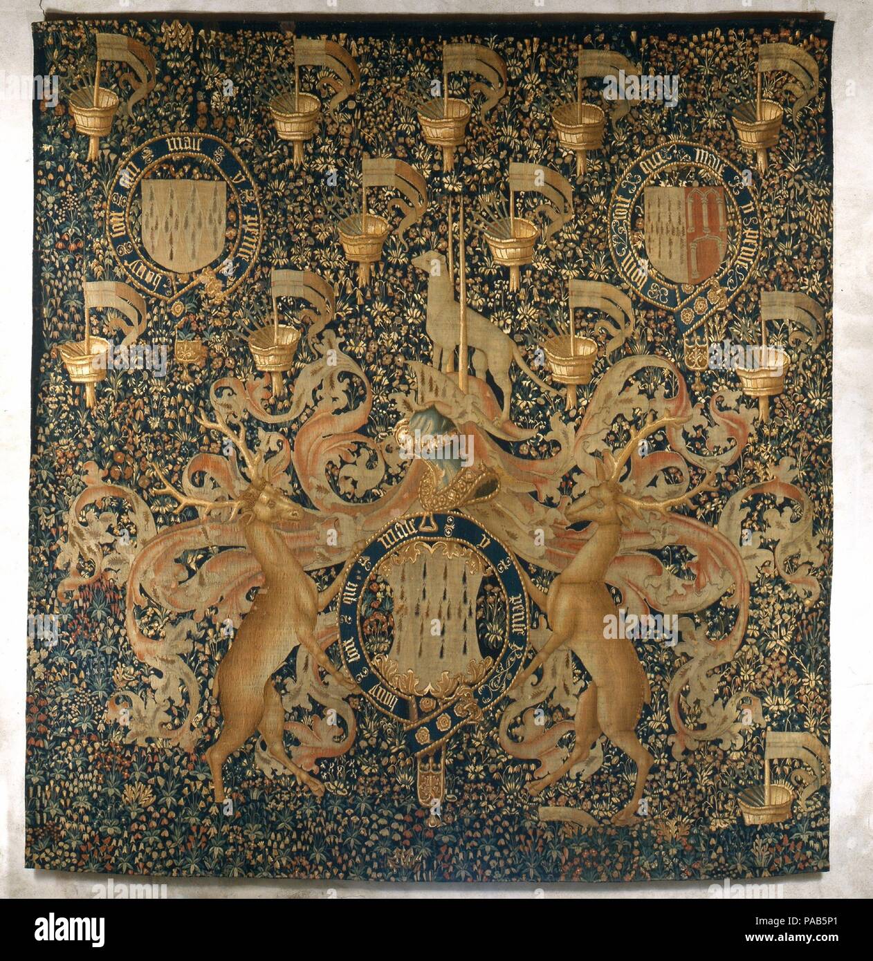 Tapestry with Armorial Bearings and Badges of John, Lord Dynham. Culture: South Netherlandish. Dimensions: 152 x 145 in.  (386.1 x 368.3 cm). Date: ca. 1488-1501.  John, Lord Dynham was a naval commander under five kings and treasurer of England from 1486 to 1501. The inscription around the garter is the motto of the Order of the Garter, to which Lord Dynham was appointed in 1487. The tapestry was probably woven to commemorate this event. The supporters in the form of stags -- or harts -- refer to Lord Dynham's family seat, Hartland. The repeated device of the topcastle of a warship with javel Stock Photo
