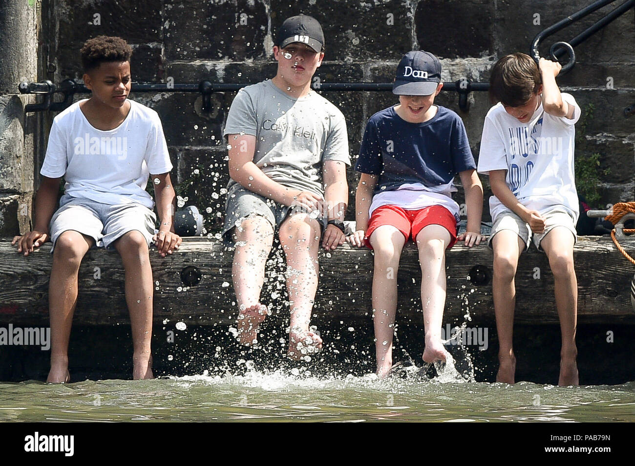 Children splash in water as they dangle their feet into Bristol's Floating Harbour during the Harbour Festival in the city centre during hot sunny weather. Stock Photo