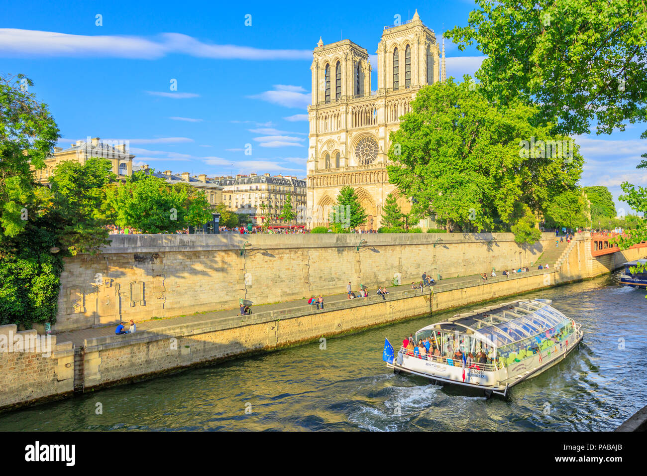 Paris, France - July 1, 2017: Bateaux-Mouches with many tourist during a trip at sunset on River Seine with Cathedral of Notre Dame on the Ile de la Cite on background. Sunny day, blue sky. Stock Photo