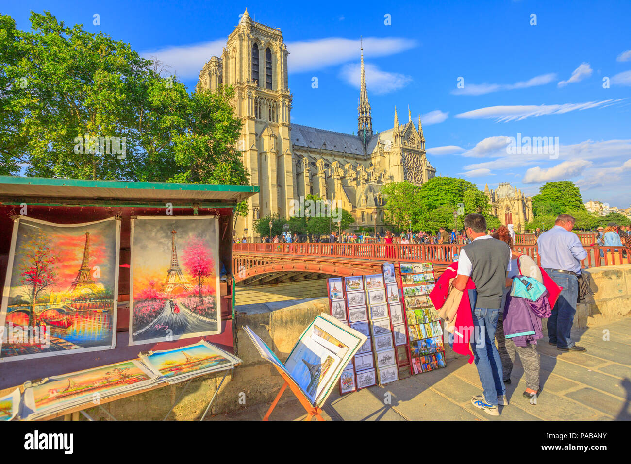 Paris, France - July 1, 2017: people looking at traditional Bouquiniste on the edge of Seine in front Notre-Dame cathedral. The Bouquinistes sell paintings of the Eiffel Tower and tourist souvenirs. Stock Photo