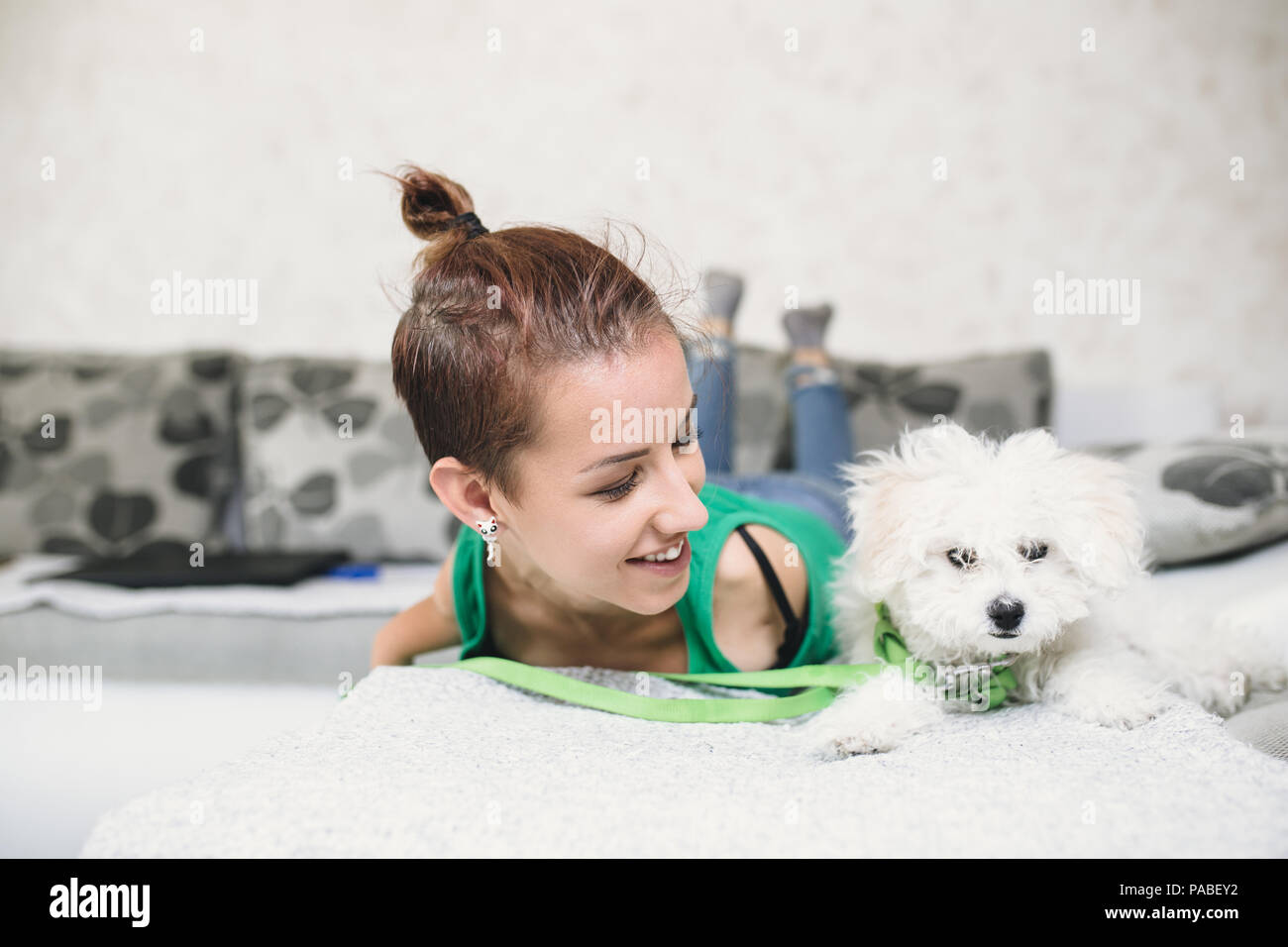 Portrait of beautiful smiling invalid young woman born without upper extremities enjoying with her little white puppy on bed. Stock Photo