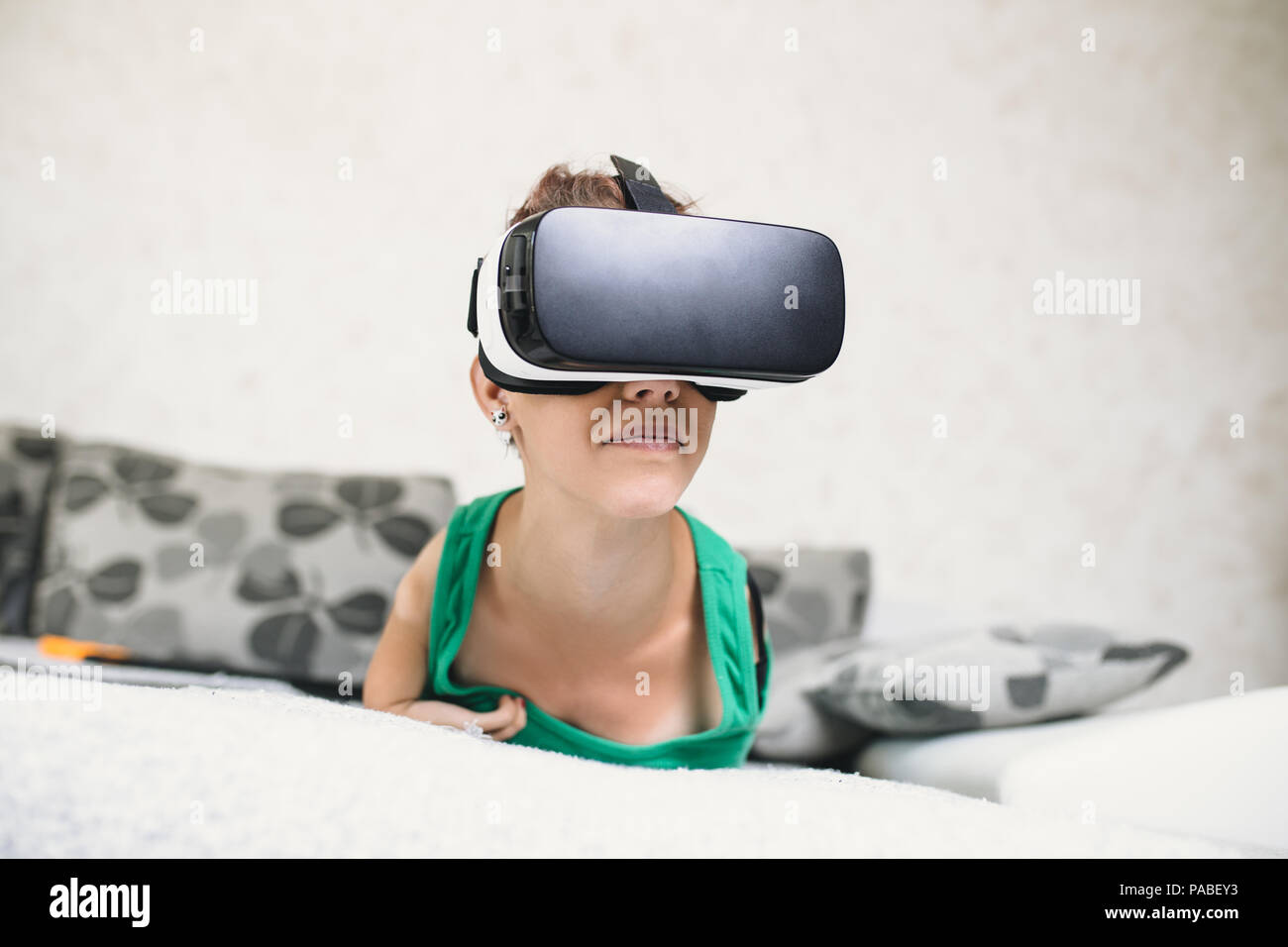 Beautiful disabled young woman with virtual reality goggles sitting on couch and preparing for playing video game. Stock Photo