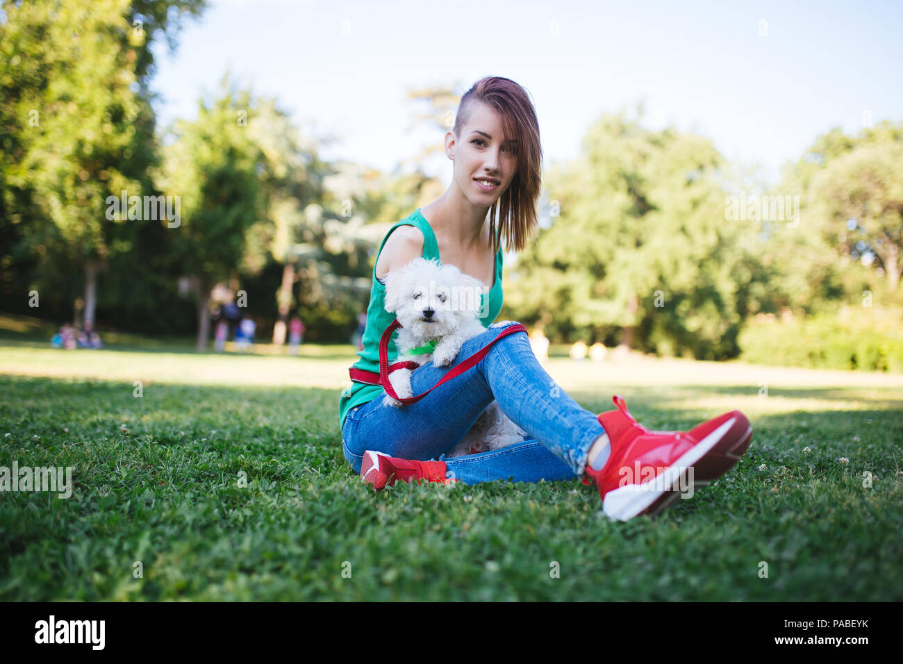 Portrait of beautiful smiling invalid young woman born without upper extremities enjoying with her little white puppy in park. Stock Photo